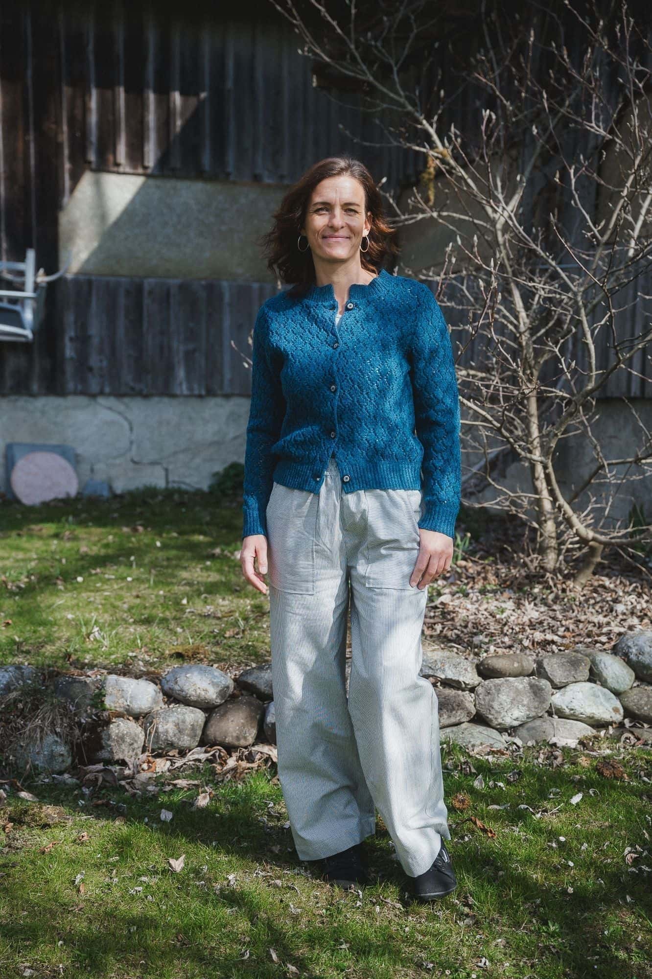 Frau trägt eine weite helle Hose mit einer blauen Strickjacke mit Ajourmuster aus Bio-Wolle vom Finkhof