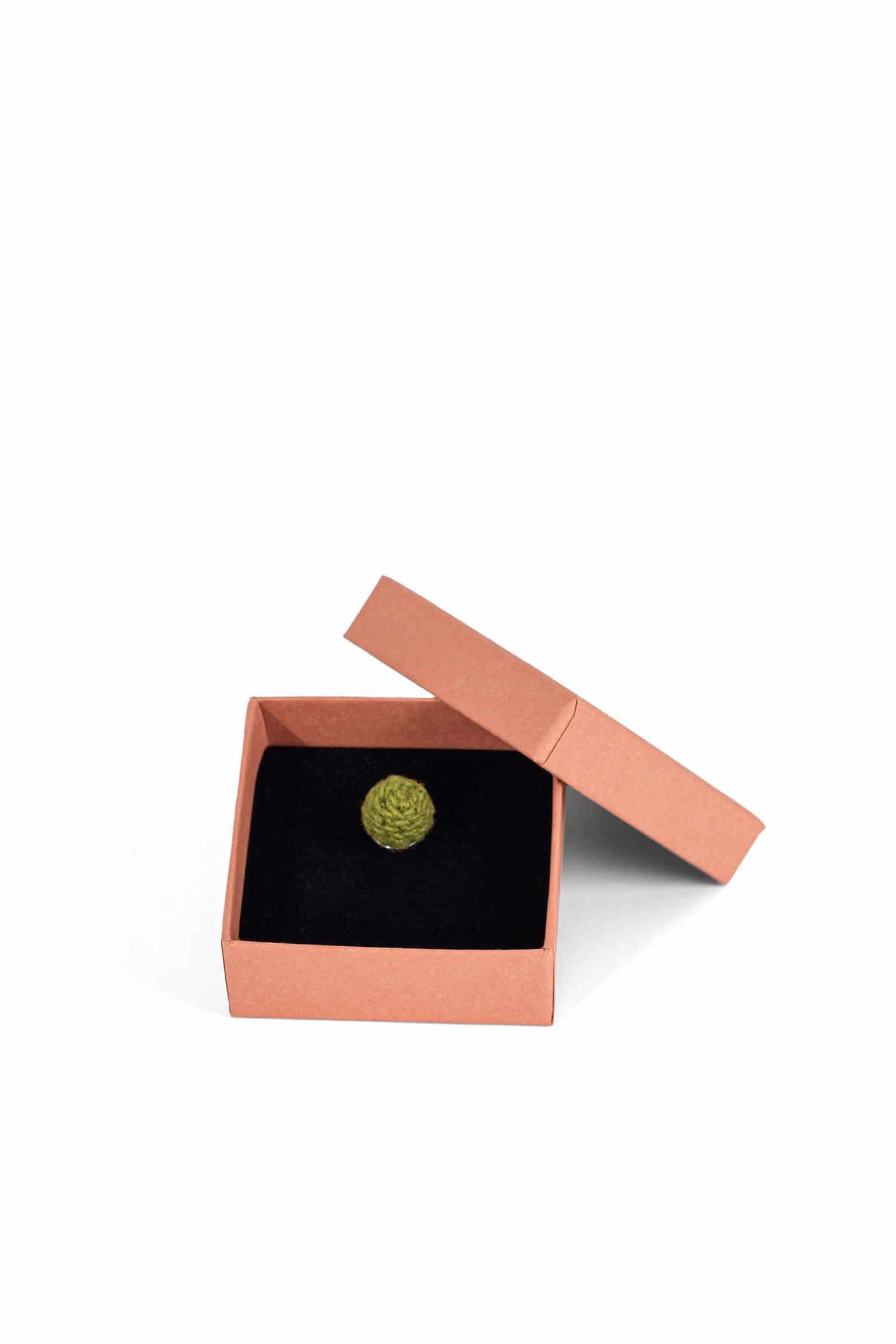 grüne handgemachte Wollperle als Kettenanhänger in lachsfarbenem Karton