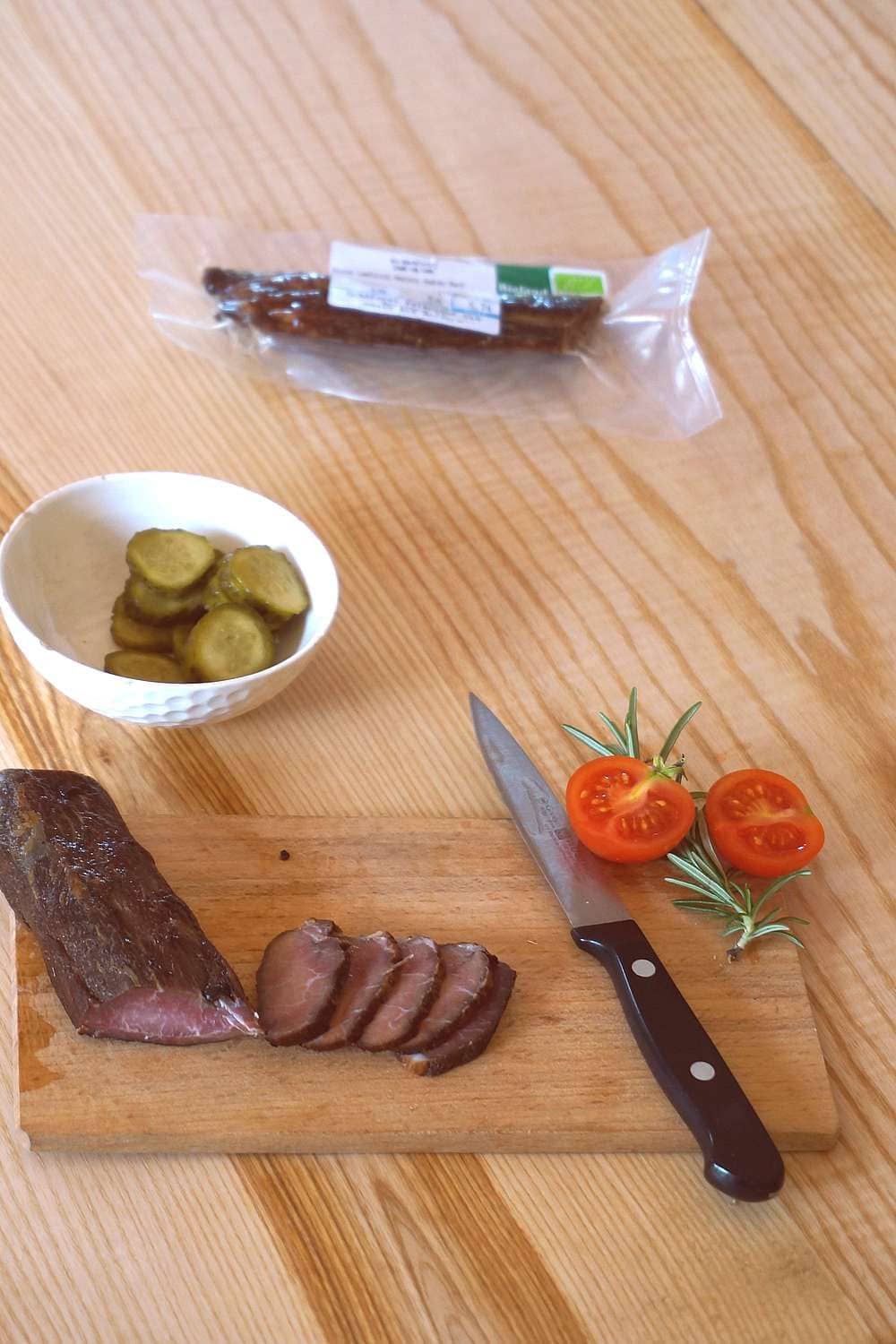aufgeschnittenes Rauchfleisch aus bio Lende vom Schaf vom Finkhof auf Holzbrett mit Tomaten und Essiggurken