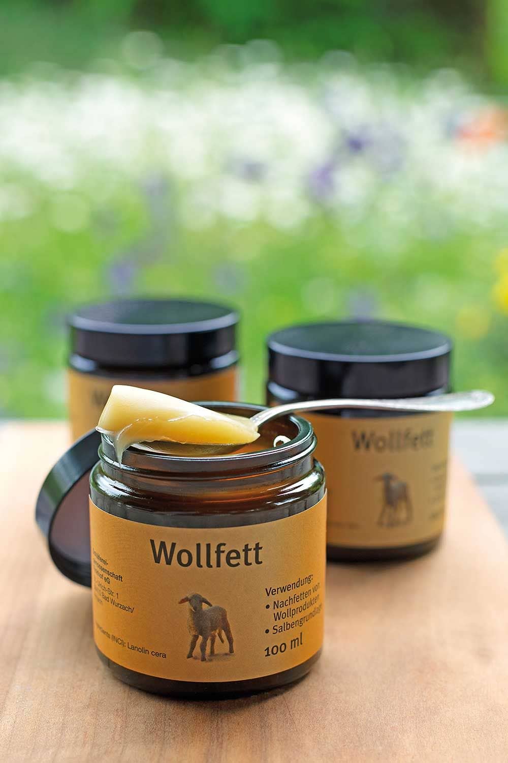 Finkhof Wollfett in braunen 100ml Glastiegeln, im Vordergrund ist ein geöffneter Tiegel mit einem Löffel Wollfett obendrauf