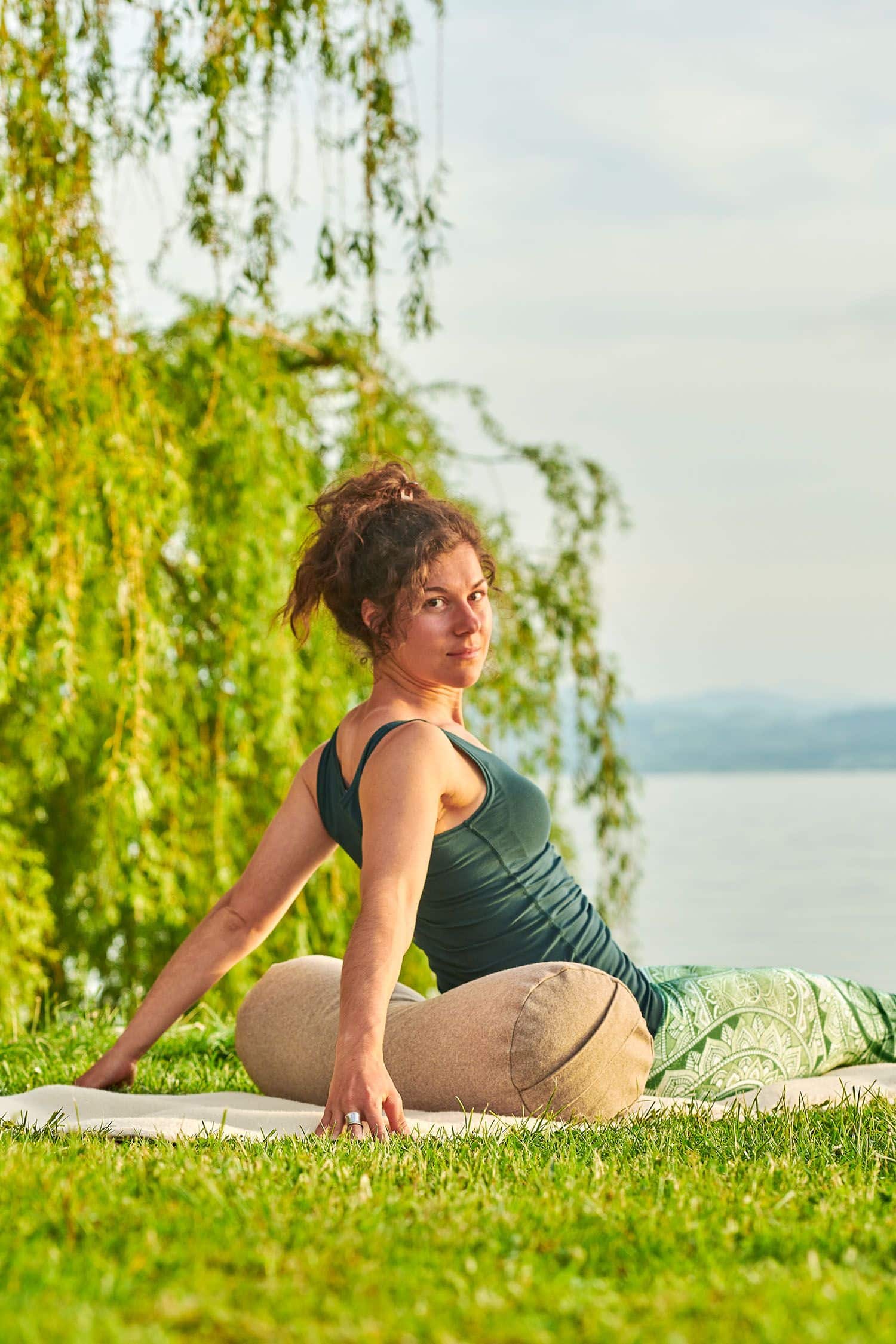 Frau sitzt in grüner Yoga Kleidung auf einer hellen Meditationsrolle aus Loden mit Dinkelspelz gefüllt vom Finkhof