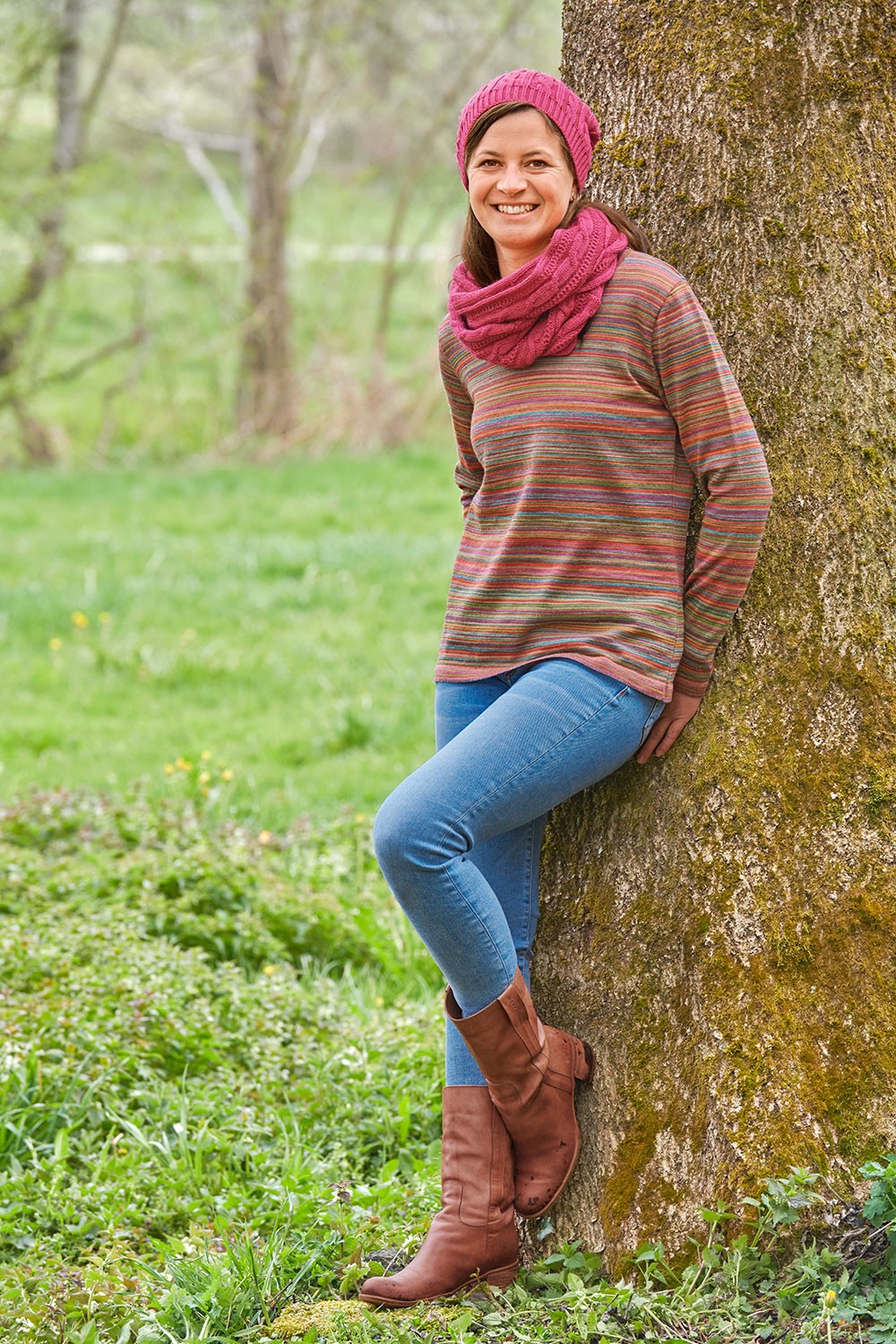 Frau mit gestreiftem Shirt, Jeans, fuchsiafarbener Mütze und pinkem Loopschal aus bio Wolle (kbT) vom Finkhof mit Zopfmuster