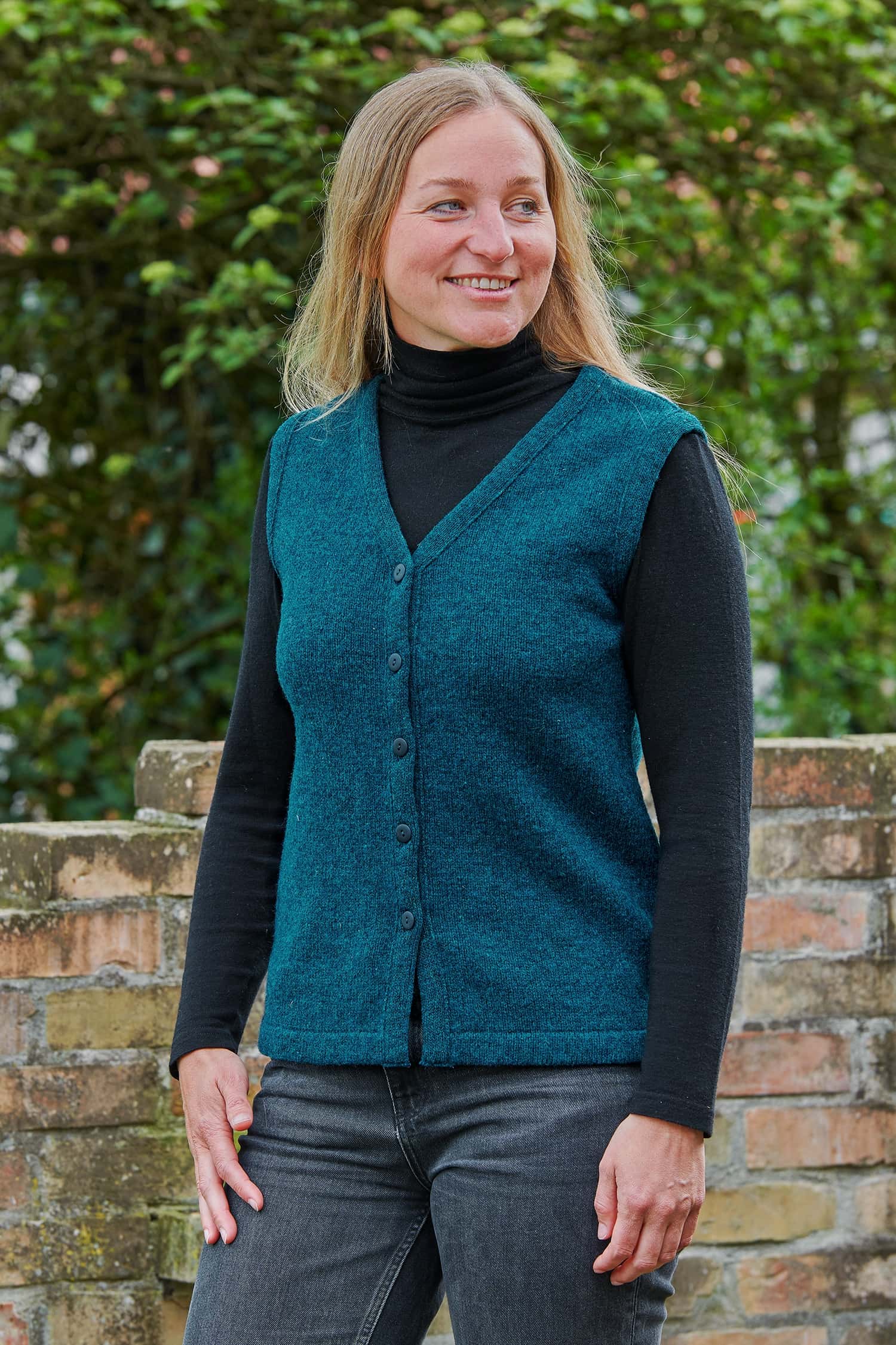 Frau mit Jeans und schwarzem Shirt trägt eine feine türkise Strickweste vom Finkhof aus Bio-Wolle