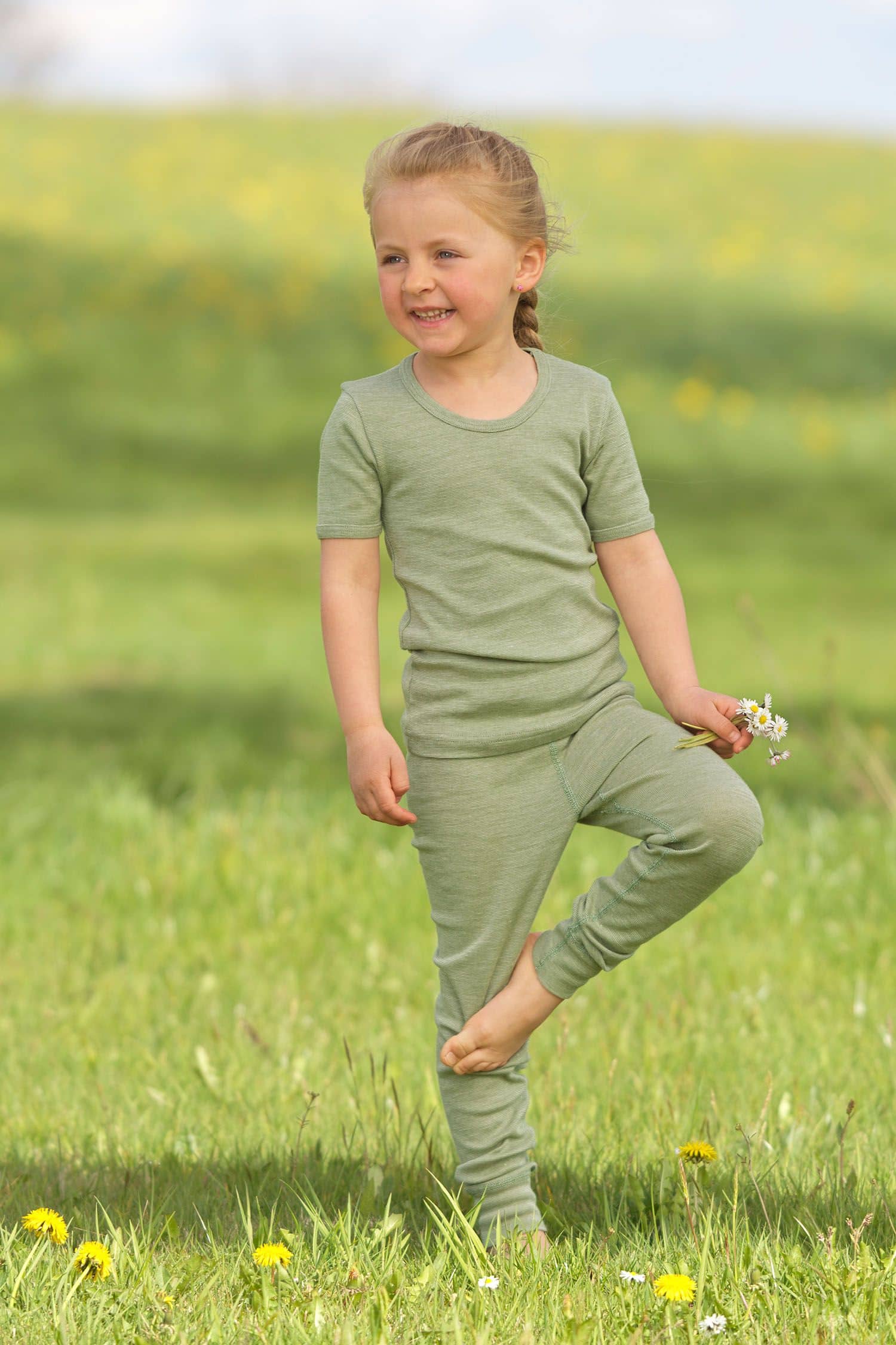 Kind spielt auf Wiese und trägt grüne lange Unterhose aus bio Wolle (kbT), bio Baumwolle (kbA) und Seide mit grünem Shirt