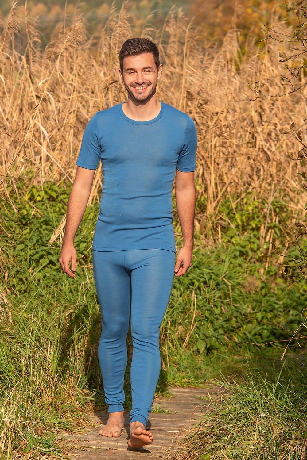 Mann läuft auf lächelnd auf Kamera zu und trägt eine blaue lange Unterhose aus bio Wolle (kbT) mit Shirt