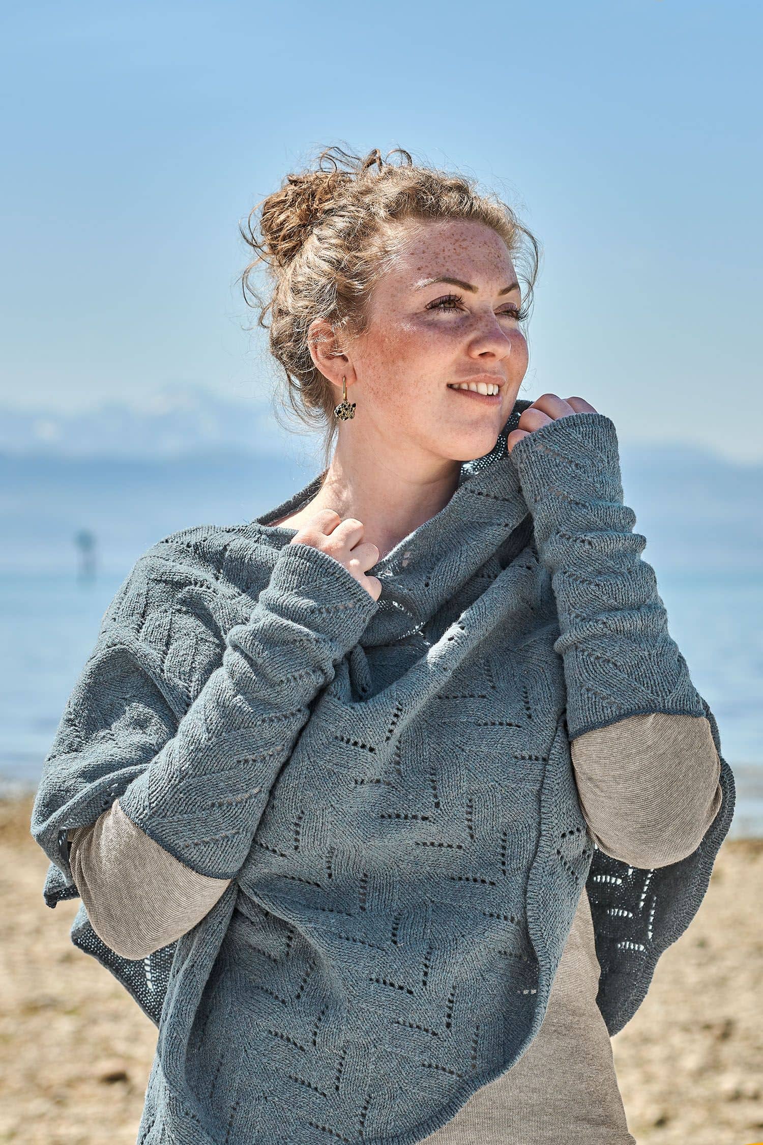 Finkhof-Ajour-Armstulpen rauchblau Frau trägt rauchblaue Armstulpen mit Ajourmuster vom Finkhof und einen passenden Poncho mit Ajourmuster