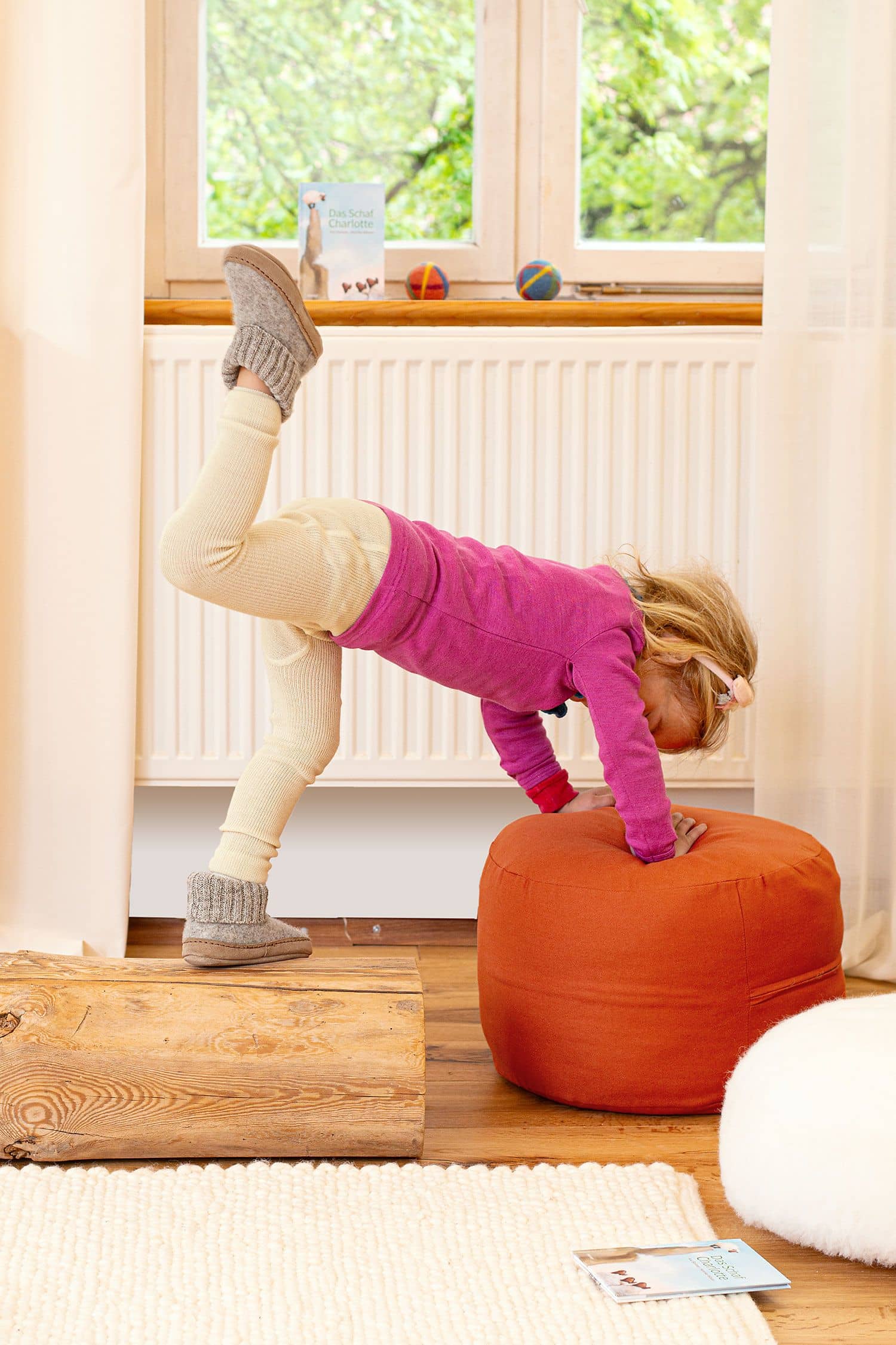Kind spielt auf Holzstamm und Sitzkissen mit Wollkleidung und Hüttenschuhen vom Finkhof aus bio Wolle (kbT)