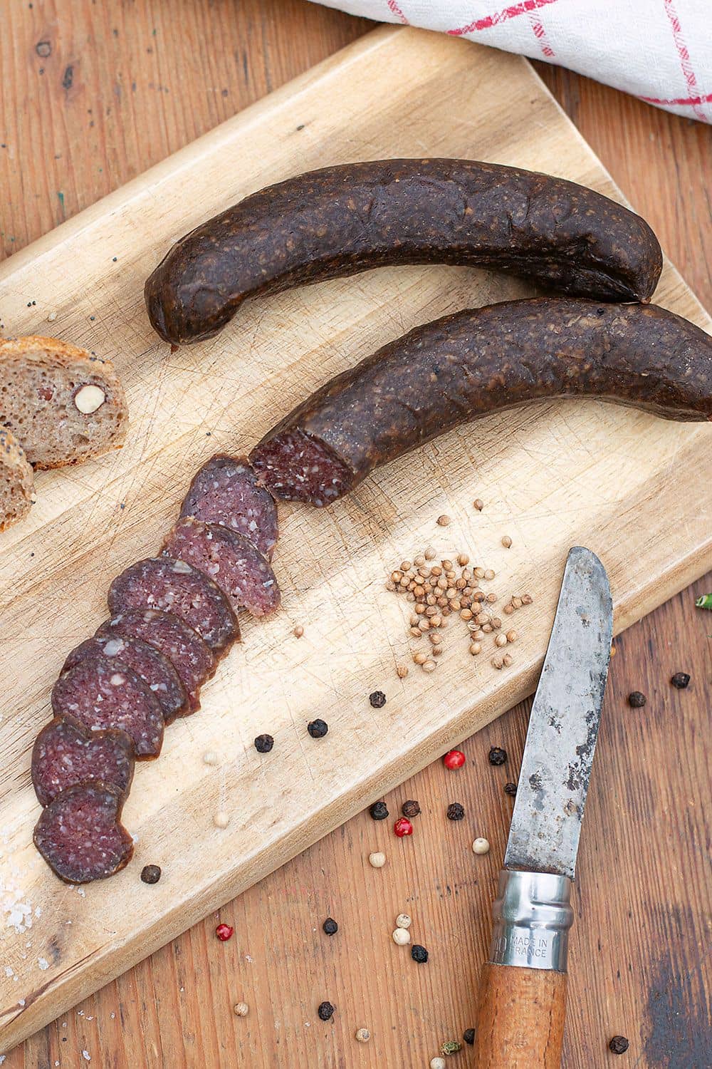 Bio-Schafsalami Bio Schafsalami vom Finkhof aufgeschnitten auf einem Brettchen mit Messer und Gewürzen daneben