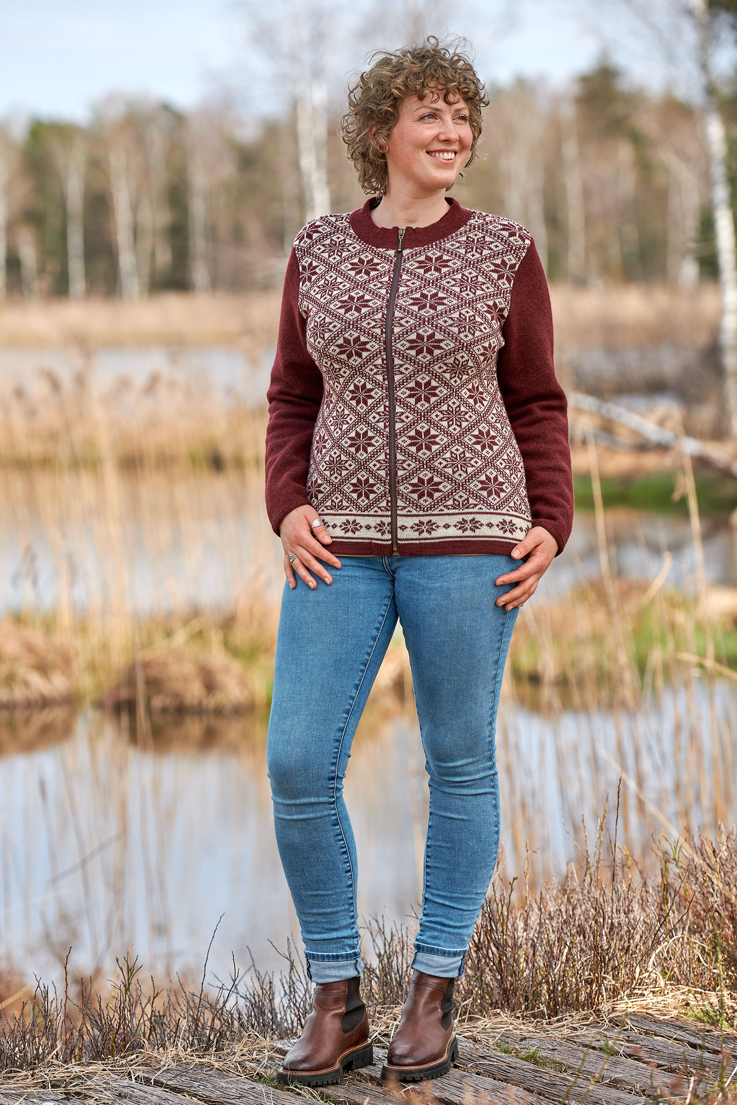 Frau mit Jeans trägt rote Jacke aus bio Wolle (kbT) mit winterlichem Muster und Jeans