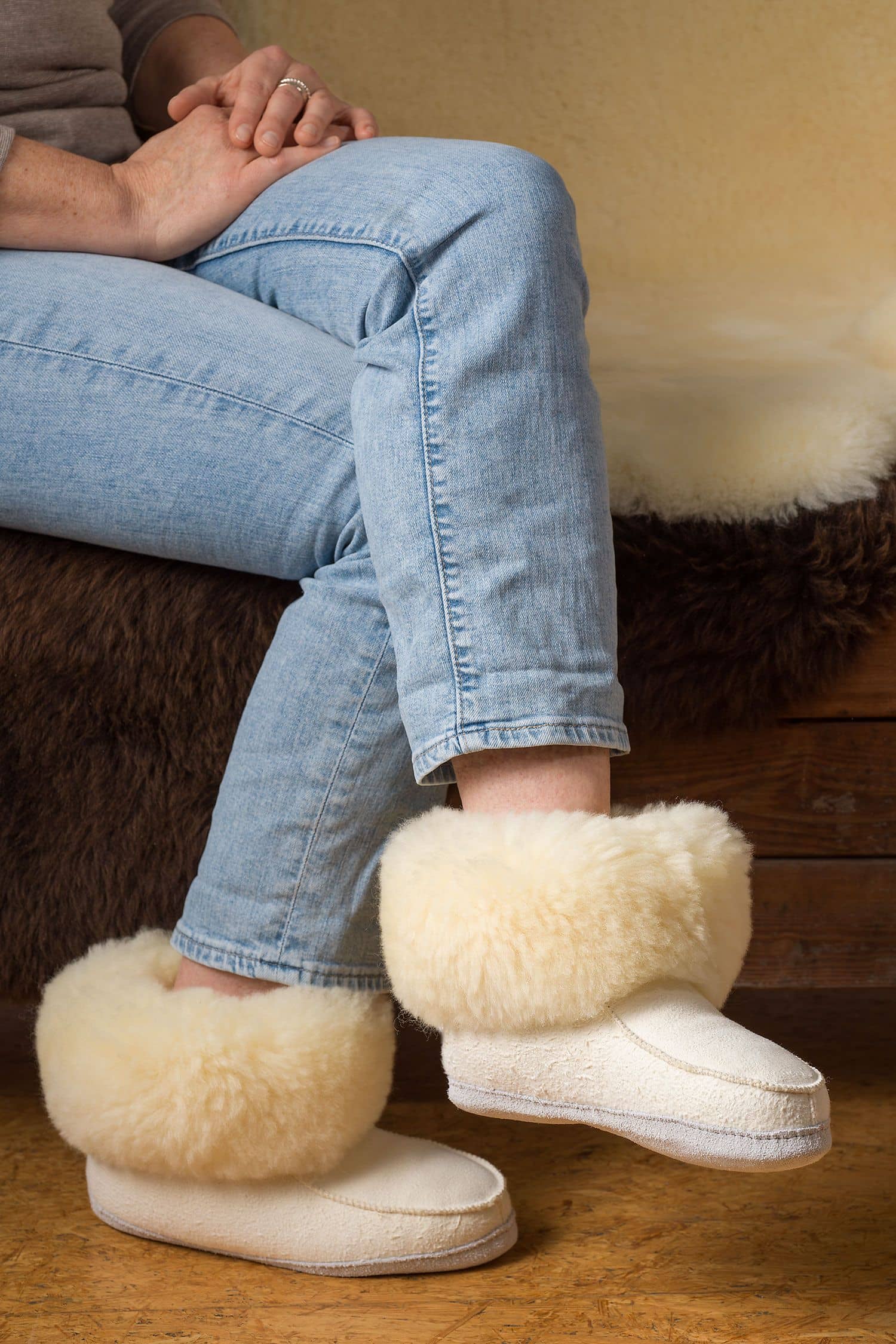 Fellschuhe relugan-gegerbt Finkhof Fellschuhe aus Relugan-gegerbtem Schaffell – getragen auf Sofa mit Fellauflage, Holzfußboden sichtbar im Hintergrund