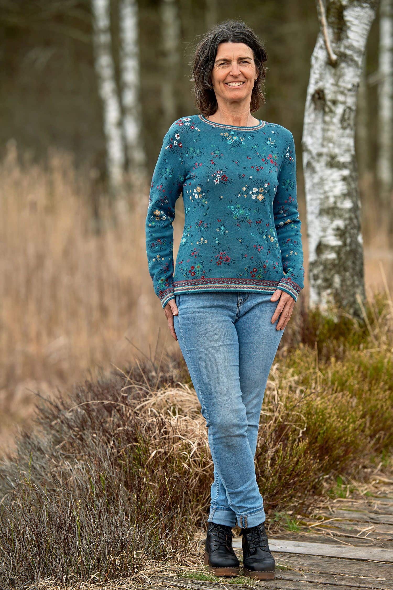 Frau auf Holzweg trägt Jeans und blau geblümten Pullover