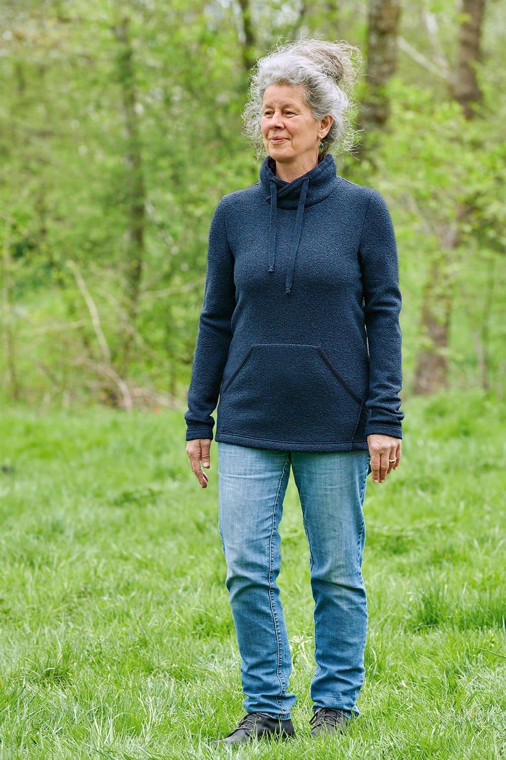 Frau läuft mit Jeans und marineblauem Pulli aus bio Wolle (kbT) über eine Wiese