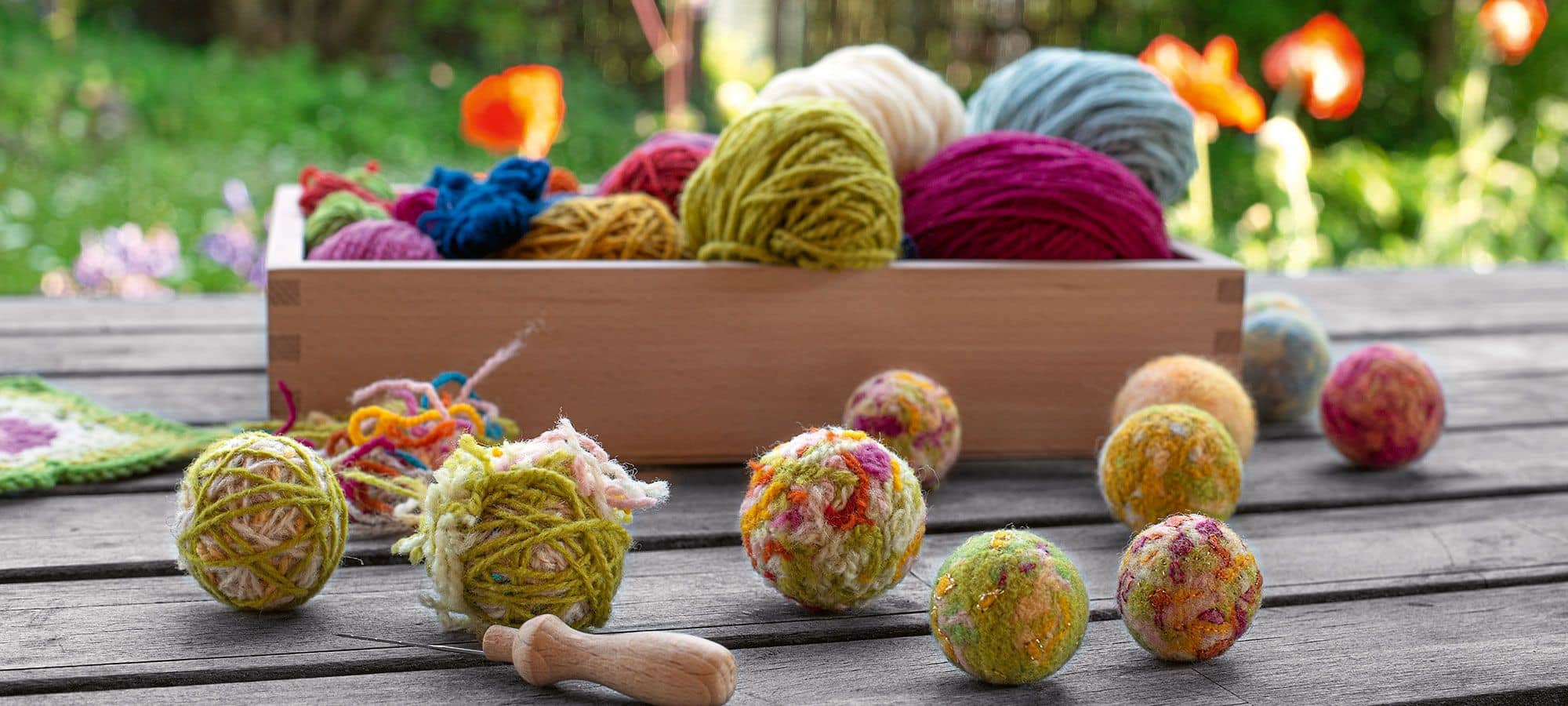 Filzkugeln in verschiedenen Größen und im Hintergrund eine Kiste mit Wollen in verschiedenen Farben