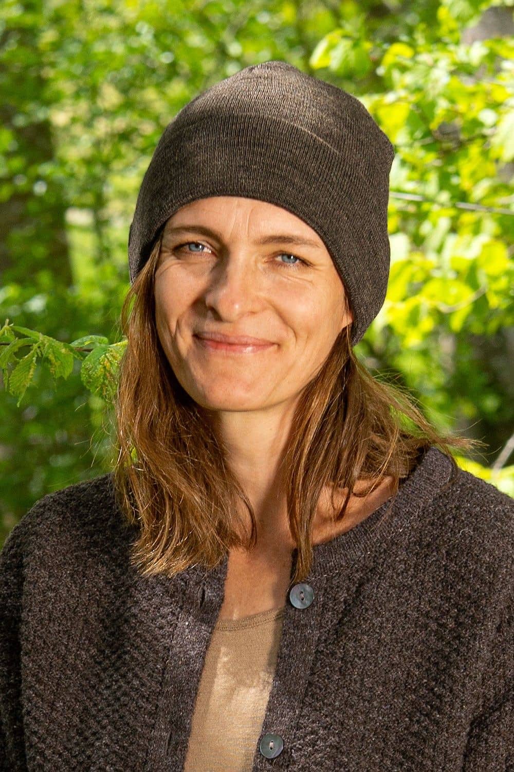 Frau mit brauner Strickjacke trägt eine braune leichte Mütze aus bio Wolle (kbT) und bio Baumwolle (kbA) vom Finkhof