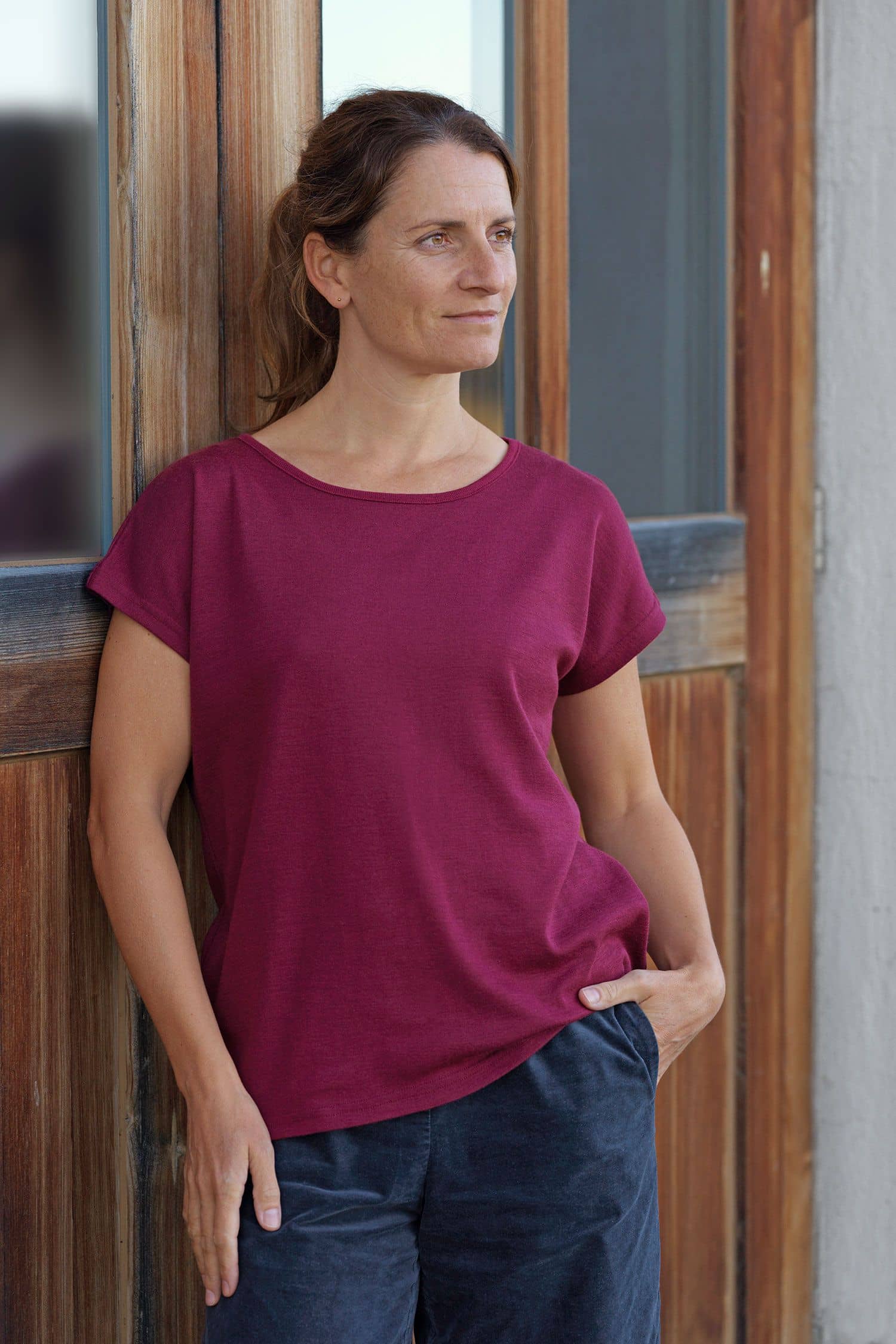 Frau trägt beerefarbenes oversize Shirt aus bio Wolle (kbT) und Seide und lehnt sich an Wand