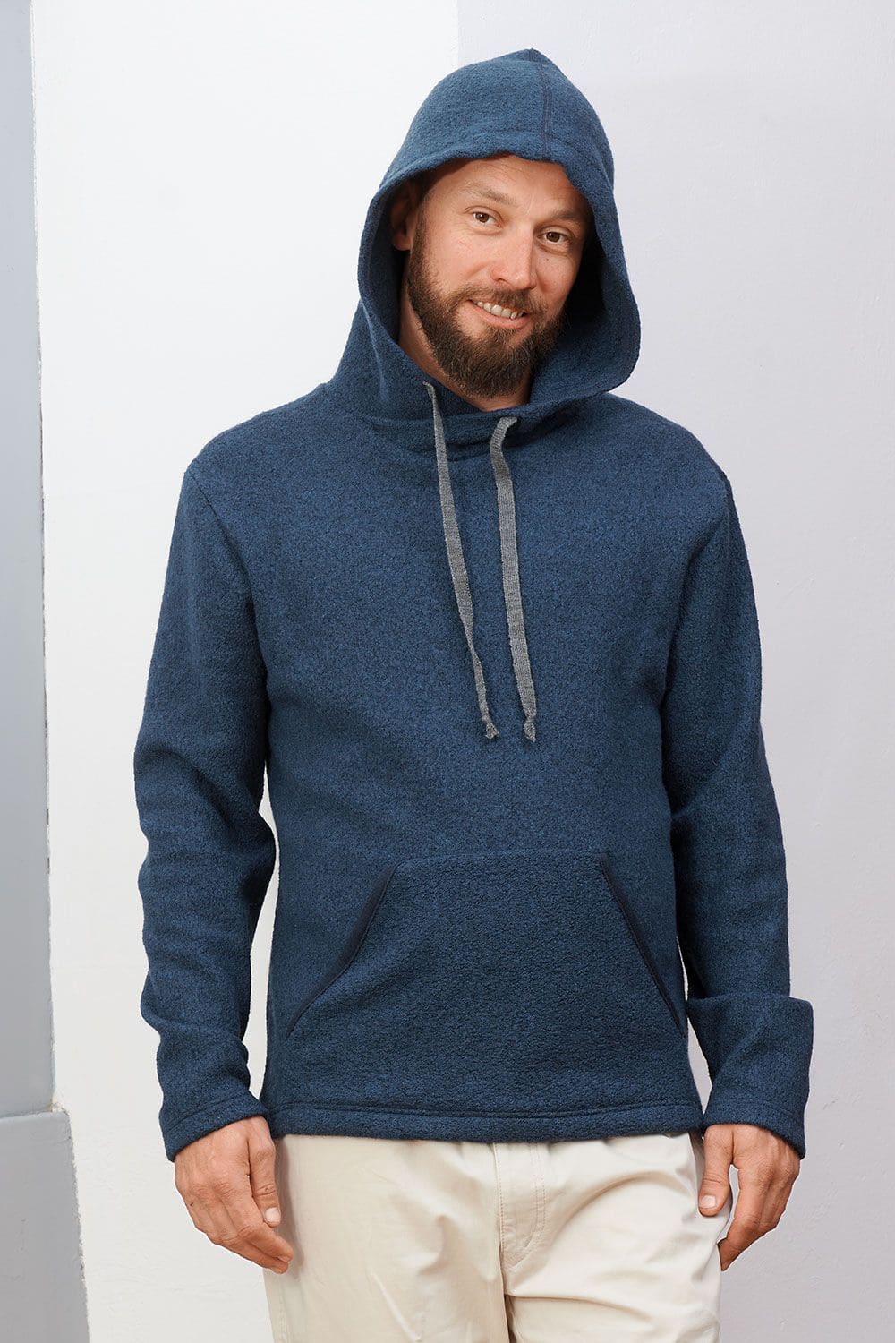 Mann steht vor Wand und trägt marineblauen Hoody aus bio Wolle (kbT) und hat Kapuze auf dem Kopf