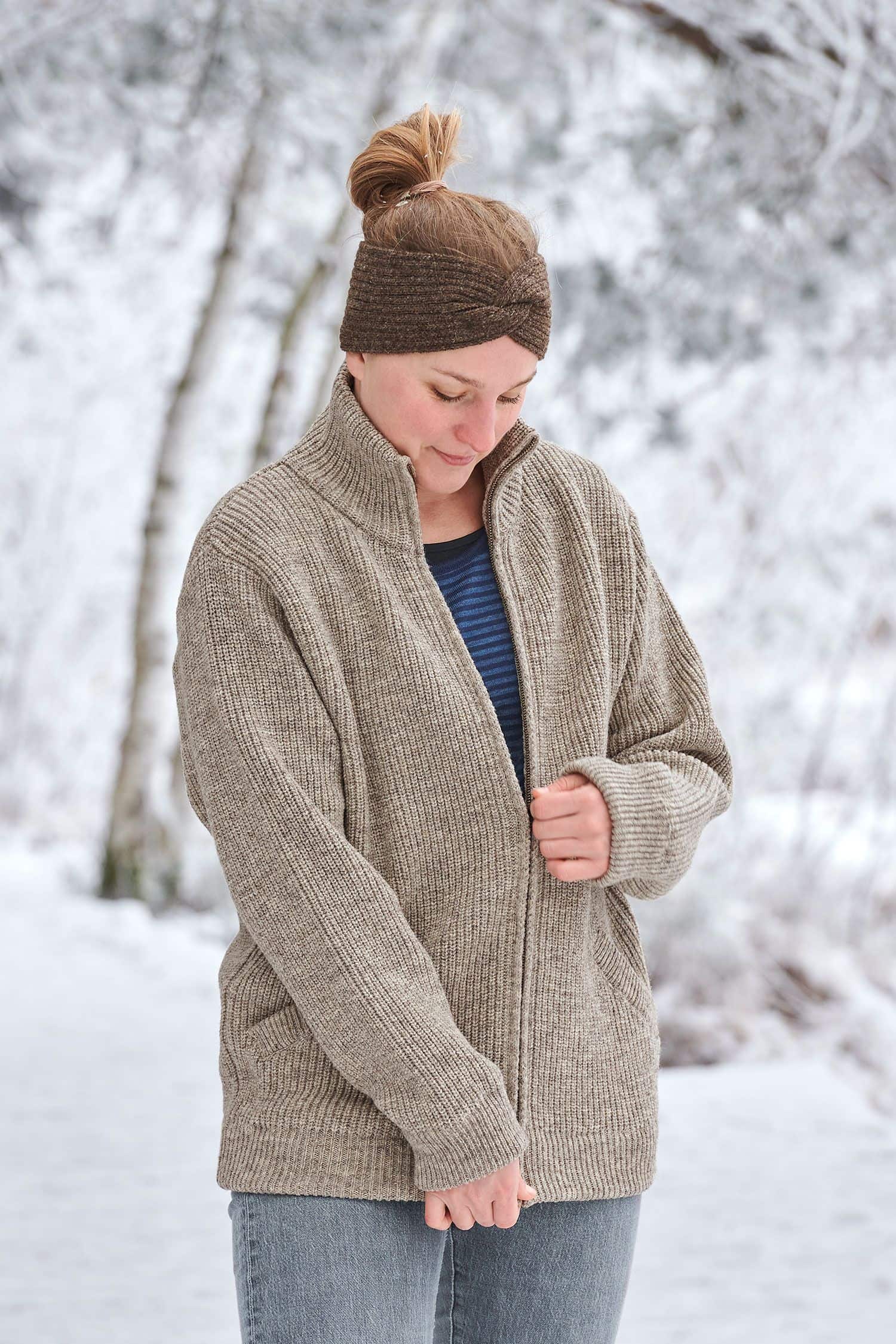 Frau in Schneelandschaft trägt graue Finkhof Jacke aus bio Wolle (kbT), braunes Stirnband mit Twist und Streifenshirt