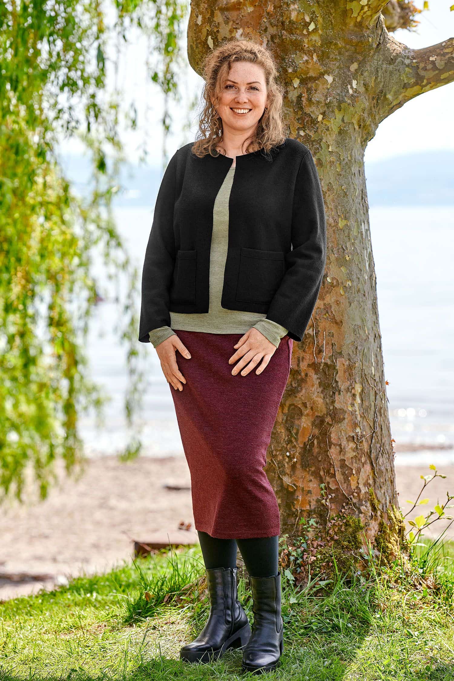 Langer Strickrock burgund Gr. M Frau trägt langen burgunderroten Strickrock aus bio Wolle (kbT), grünes Shirt und schwarze Jacke