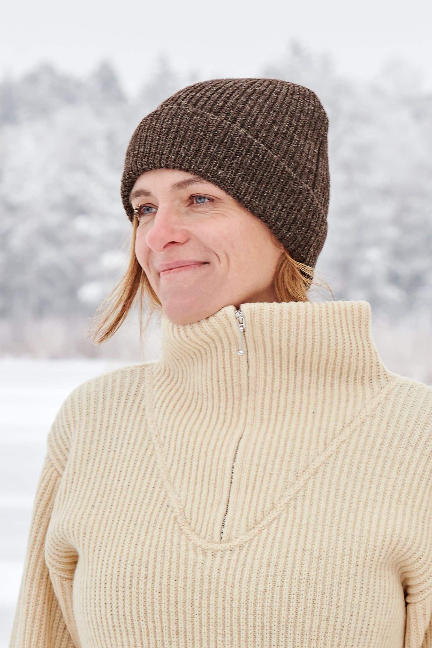 Frau trägt naturweißen Finkhof Troyer und eine braune Mütze aus bio Wolle (kbT) vom Finkhof