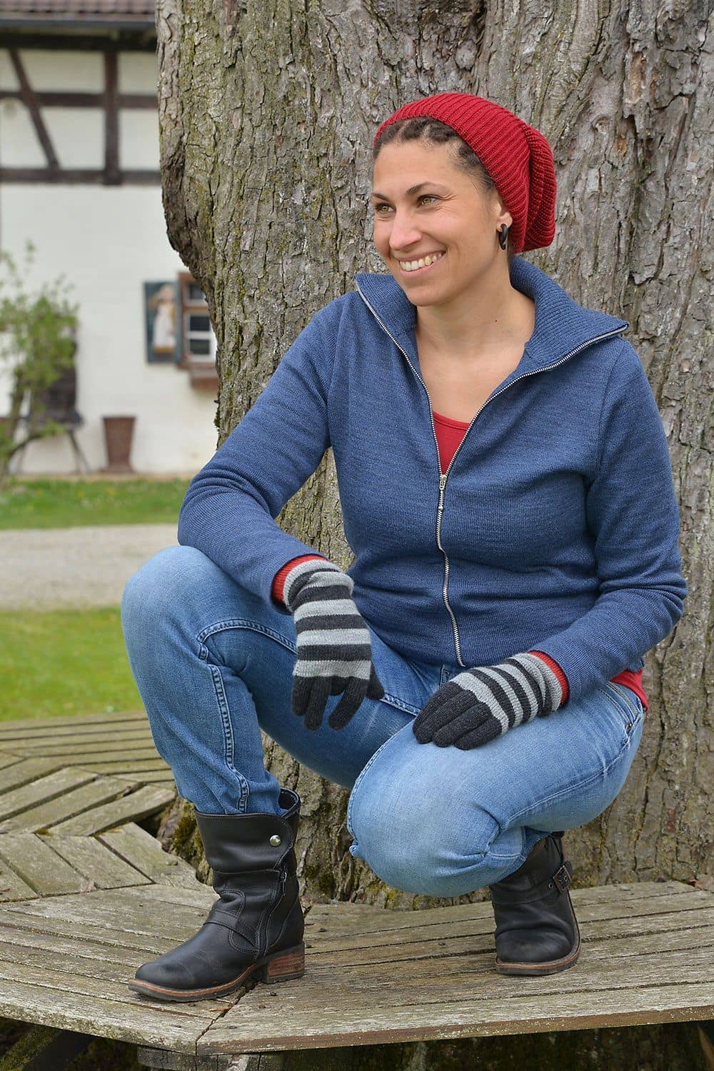 Frau kniet auf einer Bank und trägt Weste, Handschuhe, Shirt und eine rote Wollmütze aus bio Wolle (kbT) vom Finkhof
