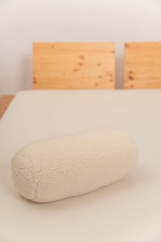 Nackenrolle mit Wollplüschbezug naturweiß Nackenrolle in naturweiß vom Finkhof mit Wollplüschbezug aus bio Wolle (kbT) auf hellem Laken mit Holzbett