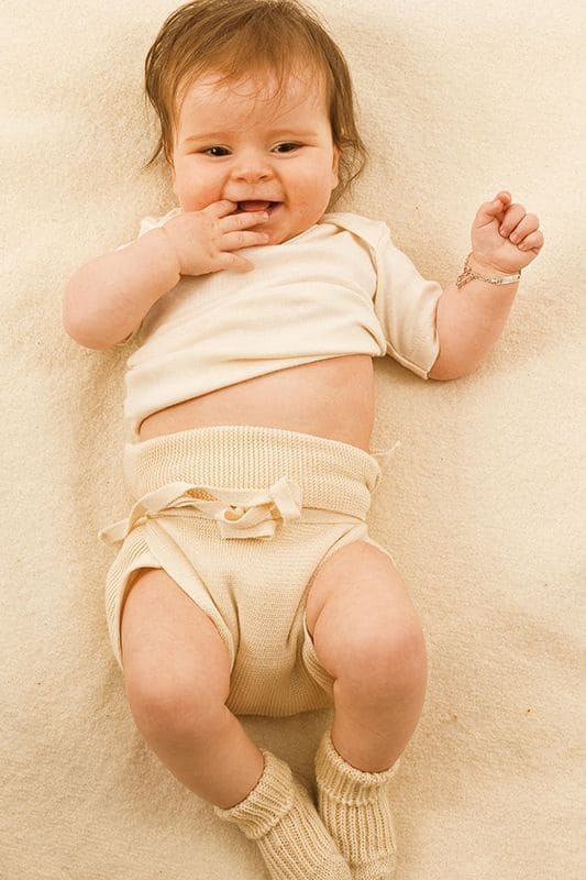 Baby mit Strickwindel aus bio Baumwolle (kbA) mit beigem Body und Stricksocken auf hellem Teppich