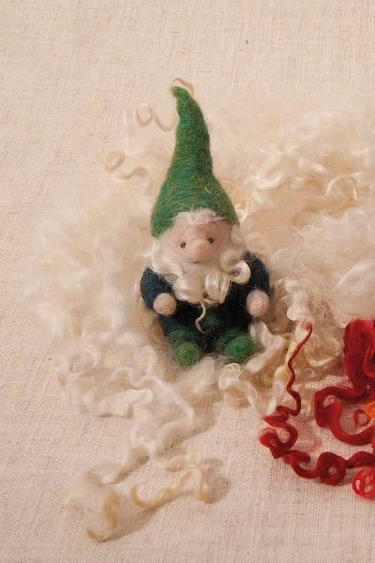 grüner Zwerg sitzt in bunten weiß roten Wolllocken auf beigem Untergrund