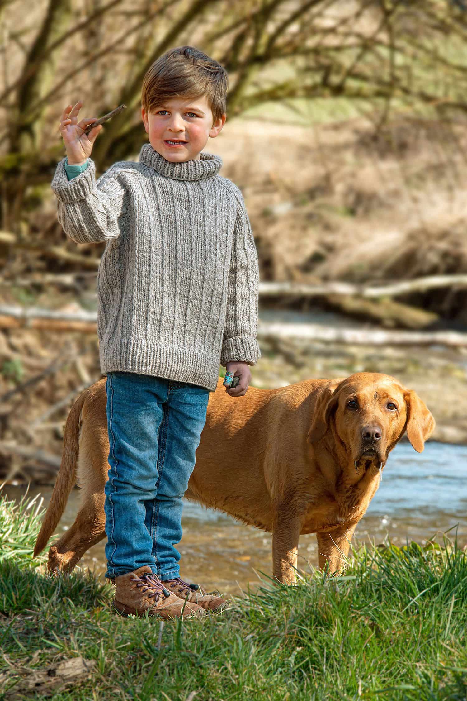 Junge trägt grauen Strickpulli als Beispiel für das Buch ,,Schnell gestrickt für Groß und Klein", brauner Hund daneben
