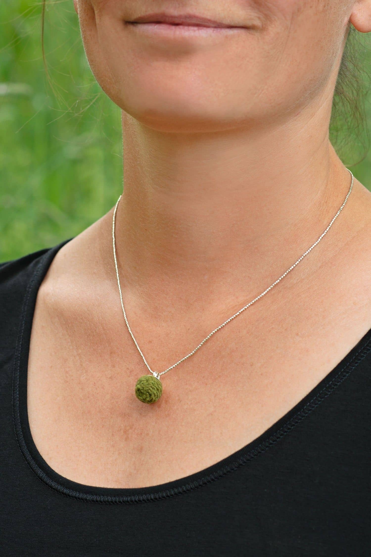 Frau mit schwarzem Shirt trägt grüne handgemachte Wollperle aus pflanzengefärbter Schurwolle