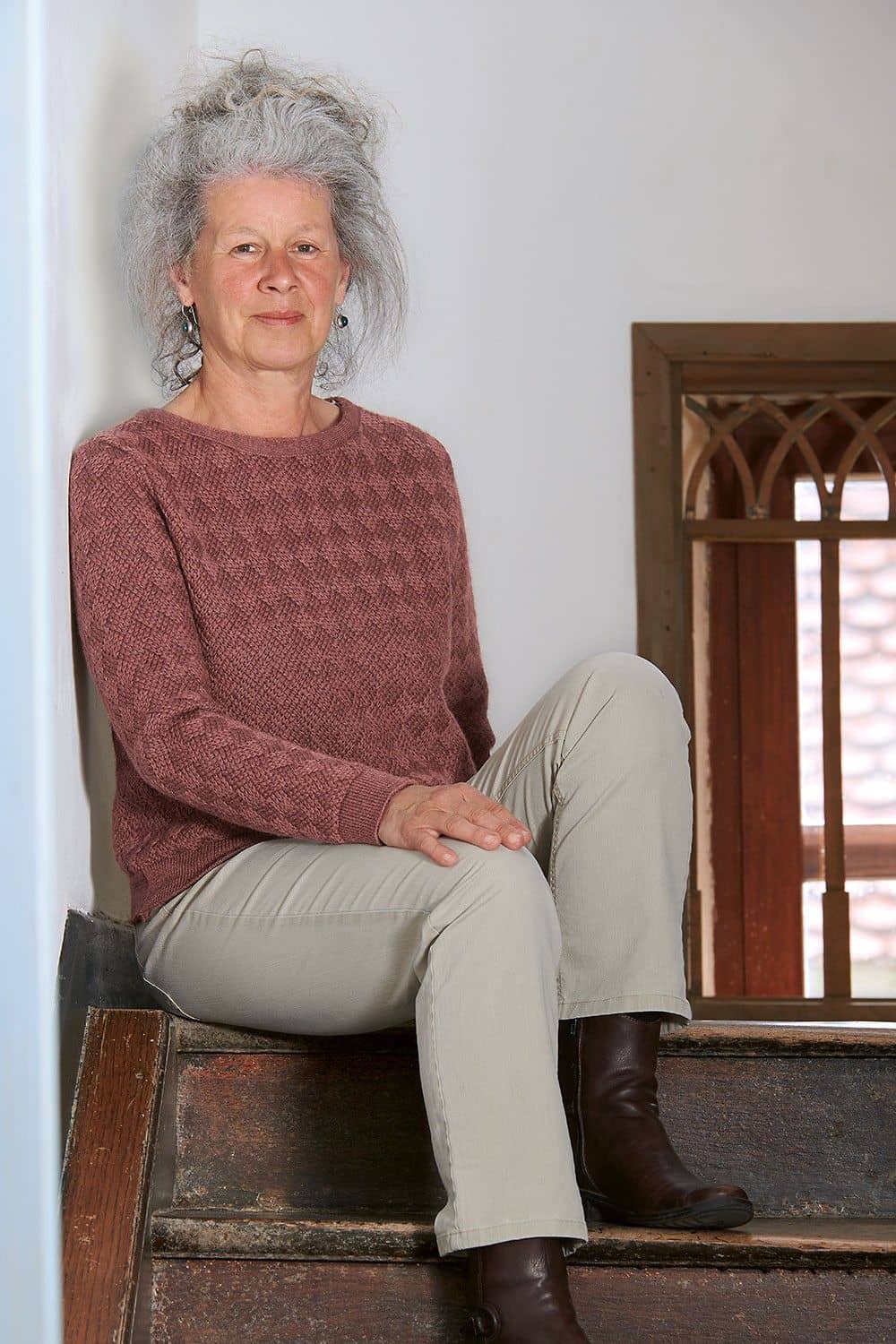 Frau sitzt auf einer Treppe und trägt altrosa Pulli mit Struktur aus bio Wolle (kbT)