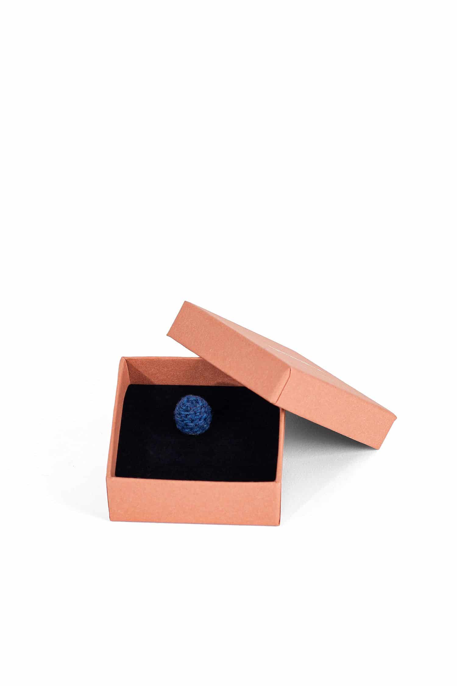 blaue handgemachte Wollperle als Kettenanhänger in lachsfarbenem Karton