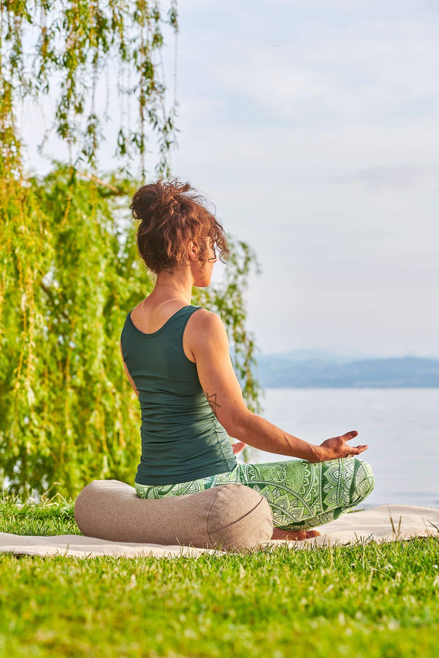 Meditationsrolle aus Loden mit Dinkelspelz Frau sitzt in grüner Yoga Kleidung auf einer hellen Meditationsrolle aus Loden mit Dinkelspelz gefüllt vom Finkhof