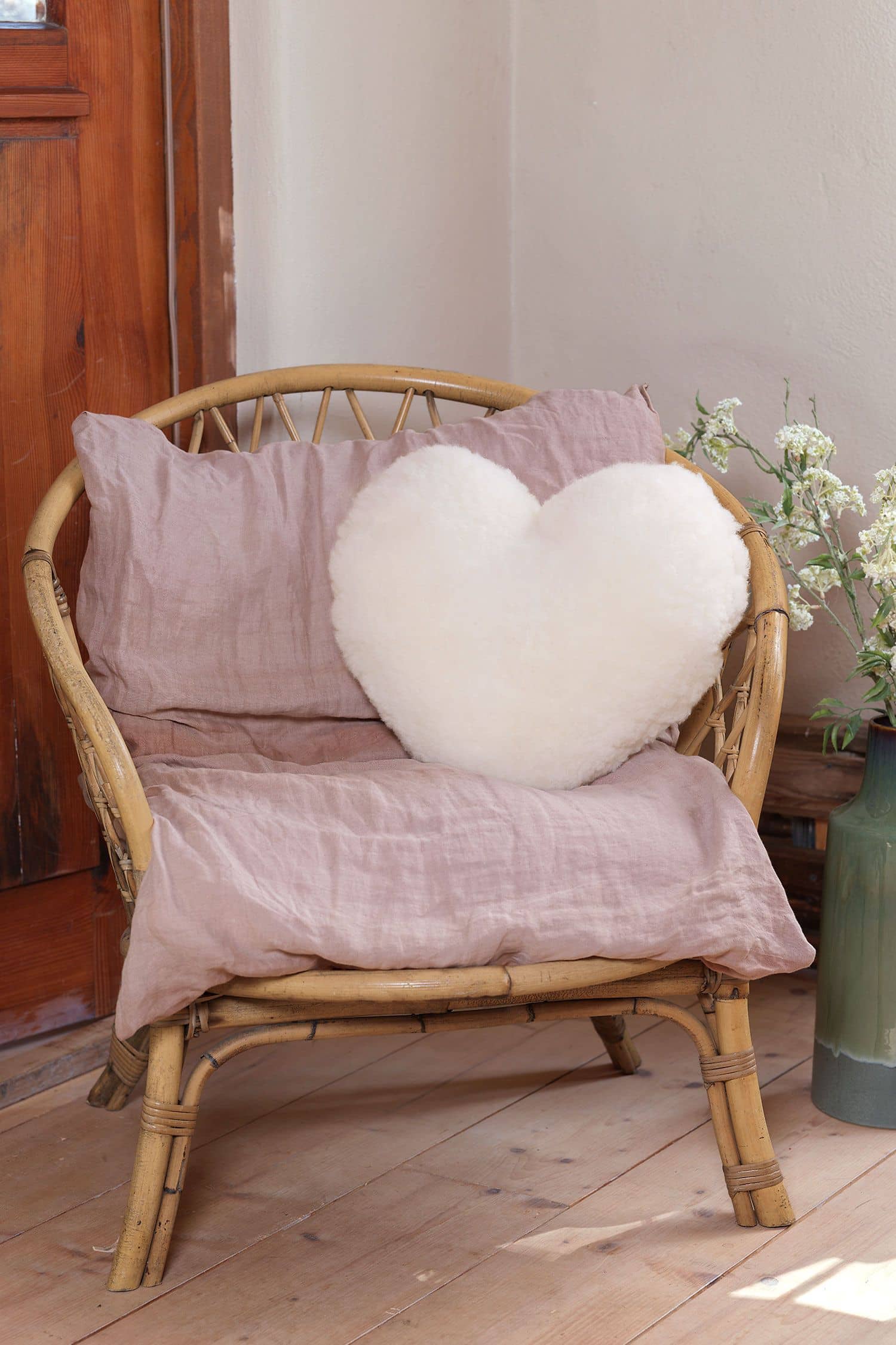 weißes Kissen in Herzform aus pflanzlich gegerbtem  Finkhof Schaffell liegt auf einem Korbstuhl