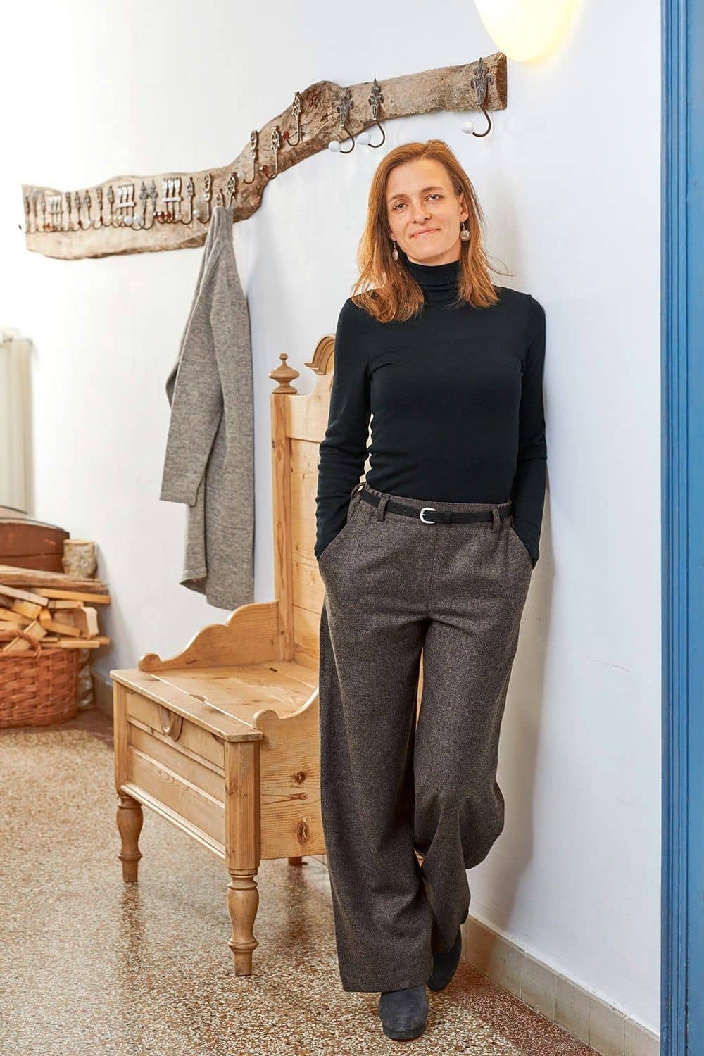 Frau lehnt an Wand und trägt braunmelierte Wollhose aus bio Wolle (kbT) vom Finkhof und einen schwarzen Unterziehrolli