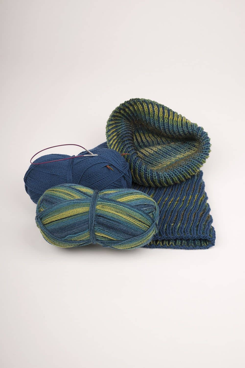 blau grüner Loopschal mit passenden Wollen daneben auf weißem Untergrund