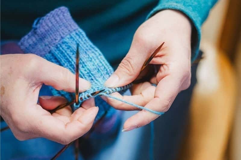 eine Frau strick ein blau lila Stück aus Finkhof Wolle