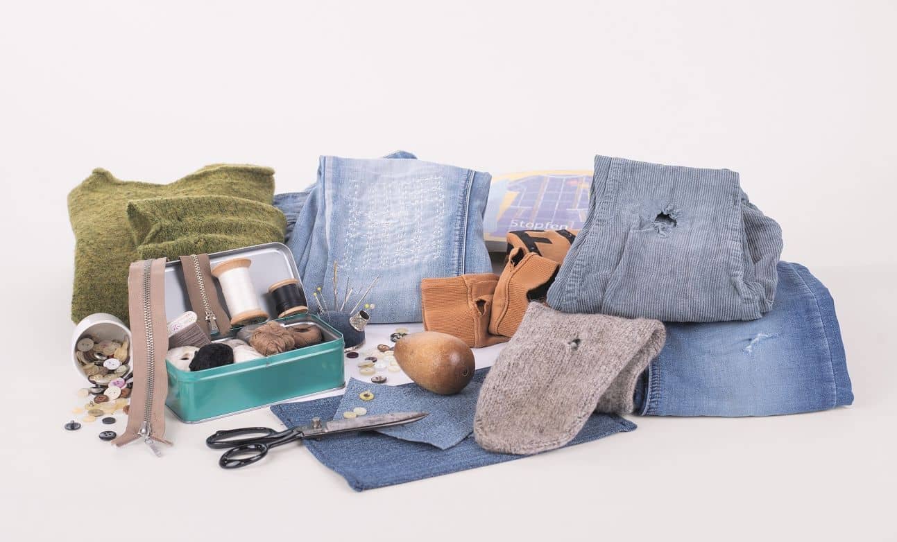 Arrangement aus Kleidung mit Löchern und Nähzubehör für das Buch ,,Flicken und Stopfen"