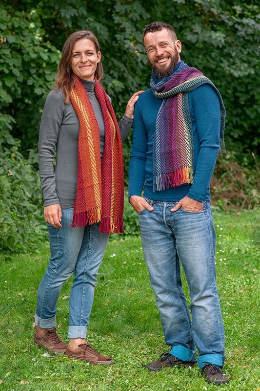 Pflanzengefärbter Wollschal handgewebt Frau und Mann mit Jeans und unifarbigem Oberteil tragen bunten pflanzengefärbten Schal vom Finkhof aus bio Wolle (kbT)