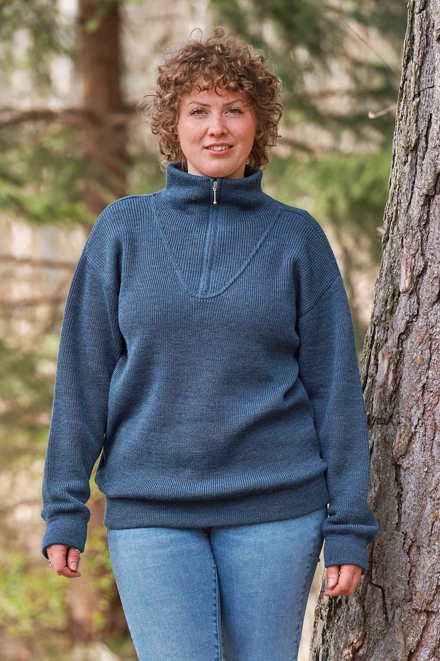 Frau lehnt mit blauem Troyer vom Finkhof aus bio Wolle (kbT) an einem Baum
