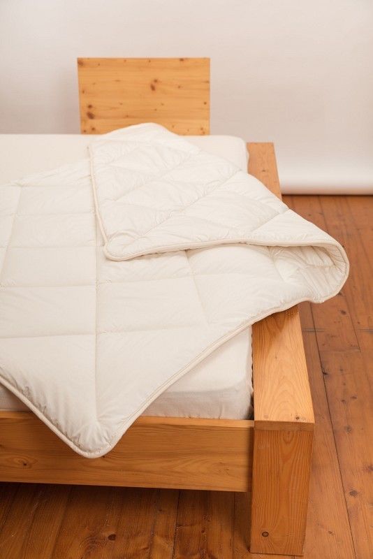 weiße Steppdecke aus bio Wolle (kbT) und bio Baumwolle (kbA) vom Finkhof auf einem braunen Bett