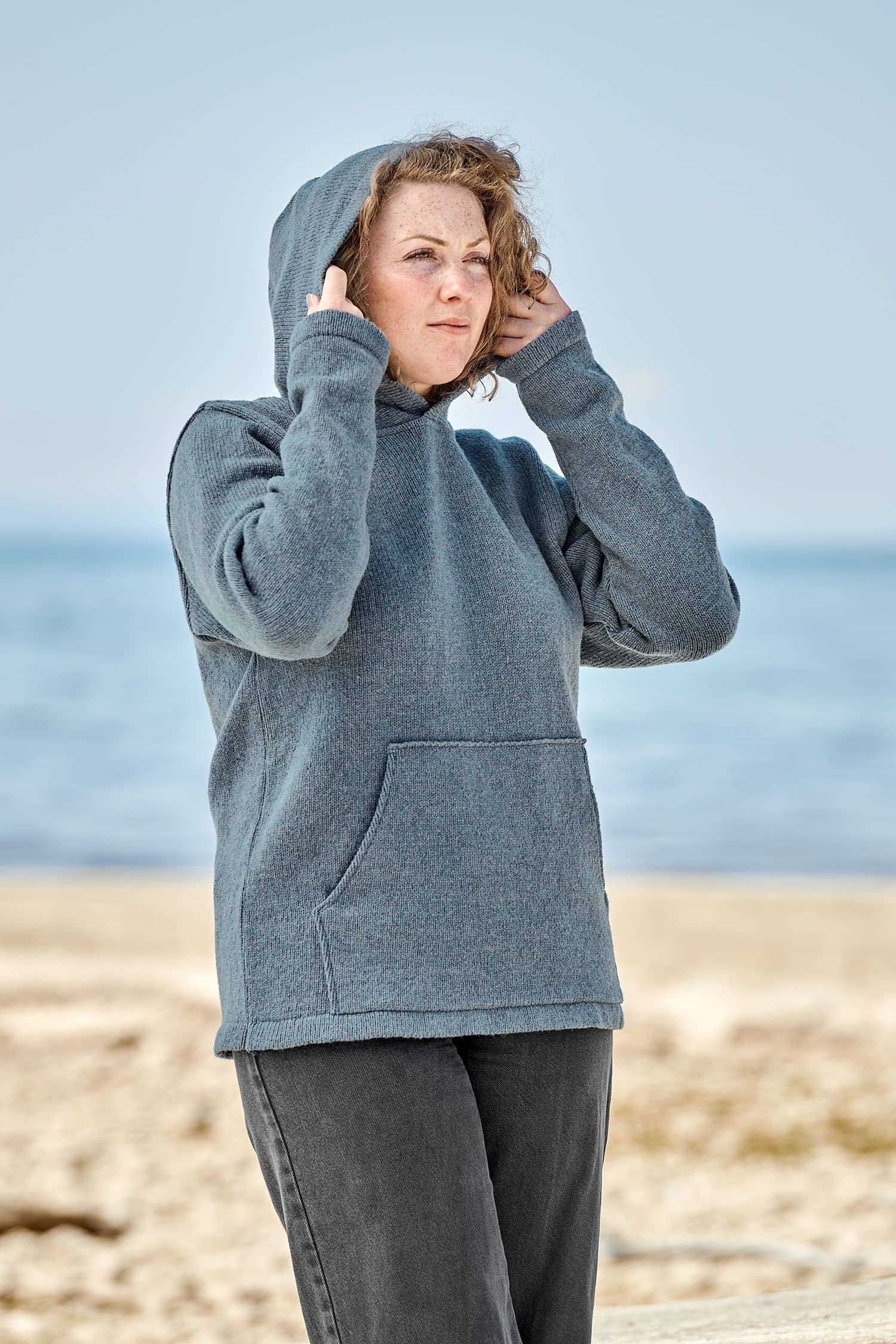 Frau setzt sich die Kapuze des rauchblauen Kapuzenpulli ausbio Merinowolle (kbT) vom Finkhof auf