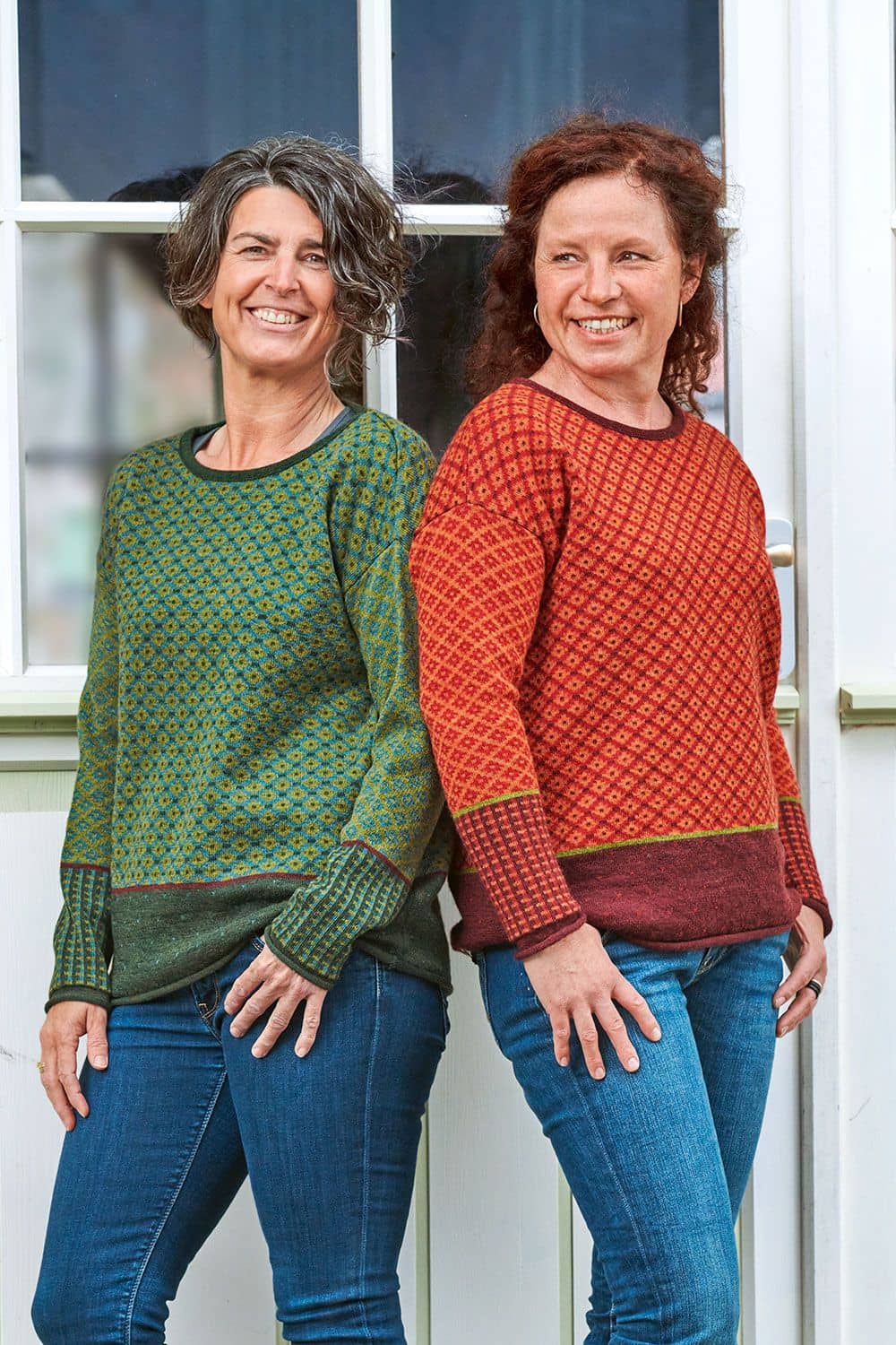 Pulli Vroni Frauen stehen Rücken an Rücken und tragen türkis und orangegemusterte Pullis aus bio Wolle (kbT) mit Jeans