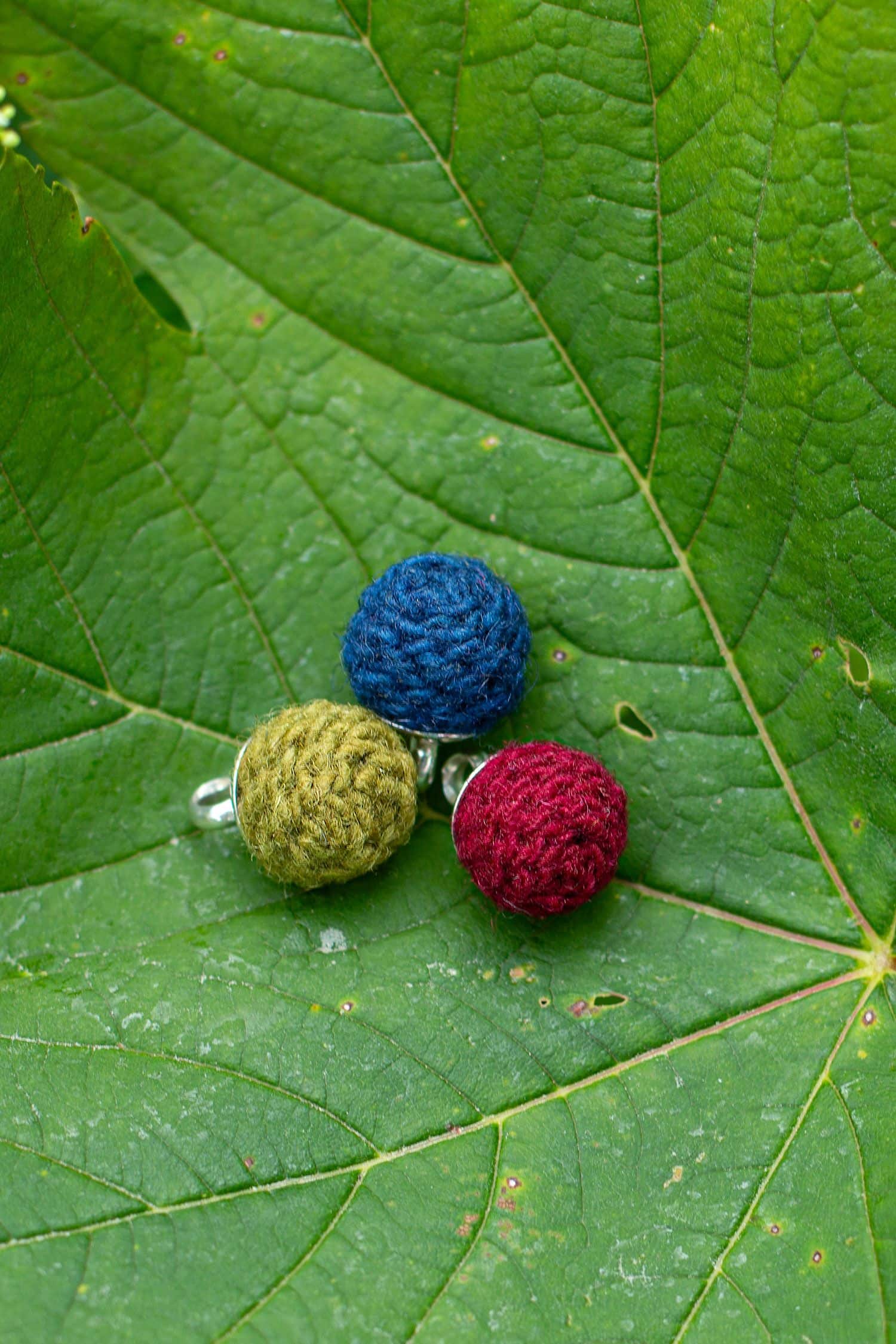 Kettenanhänger Wollperle handgemacht lindgrüne, blaue und rote handgemachte Wollperle als Kettenanhänger liegen auf grünem Blatt