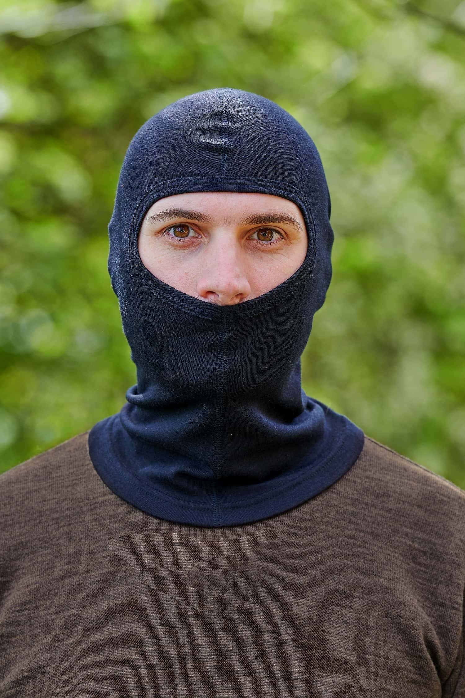 Mann mit braunem Pullover trägt eine schwarze Sturmhaube aus Bio-Schurwolle und Seide