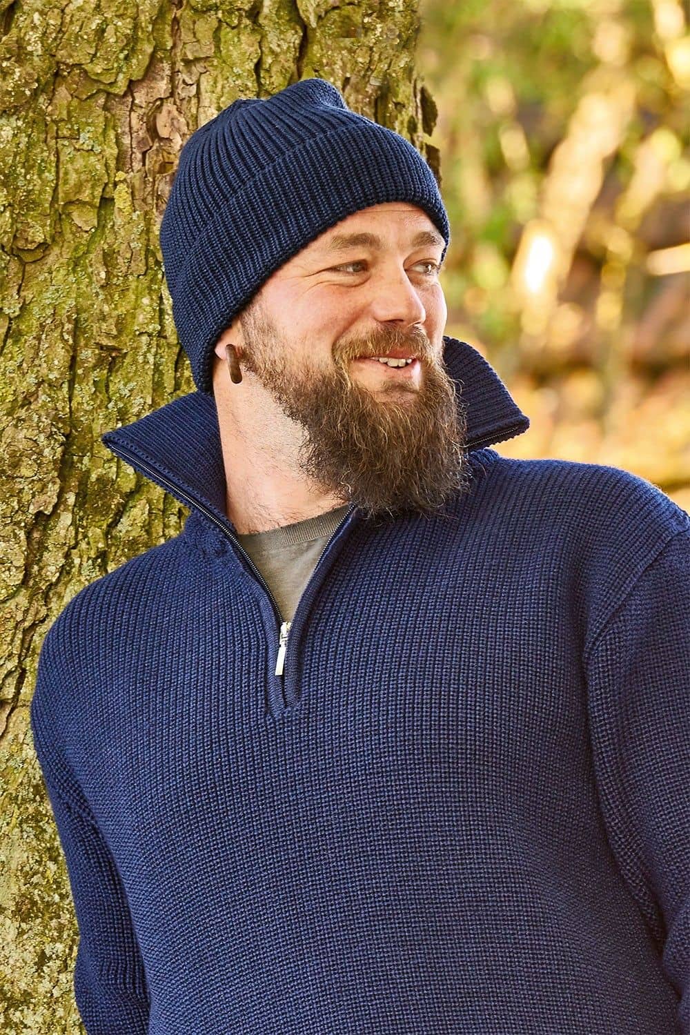 Wollmütze marine Mann mit blauem Troyer lehnt sich an Baum und trägt eine marineblaue Finkhof Wollmütze aus bio Woll (kbT)