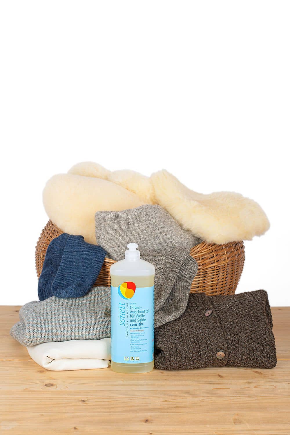 Olivenwaschmittel für Wolle und Seide - sensitiv 1000 ml Olivenwaschmittel sensitiv in ein Liter Flasche für Wolle und Seide mit Wäsche im Korb im Hintergrund