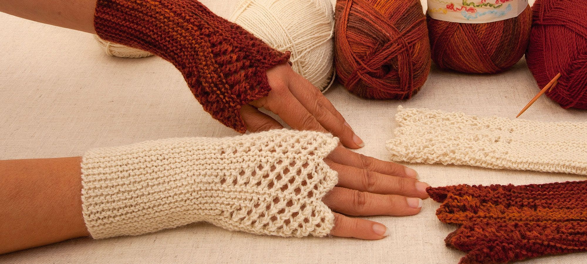 Strickanleitung Stulpen mit Zackenrand Frau trägt orange und weiße Strickstulpen und Wollknäulen