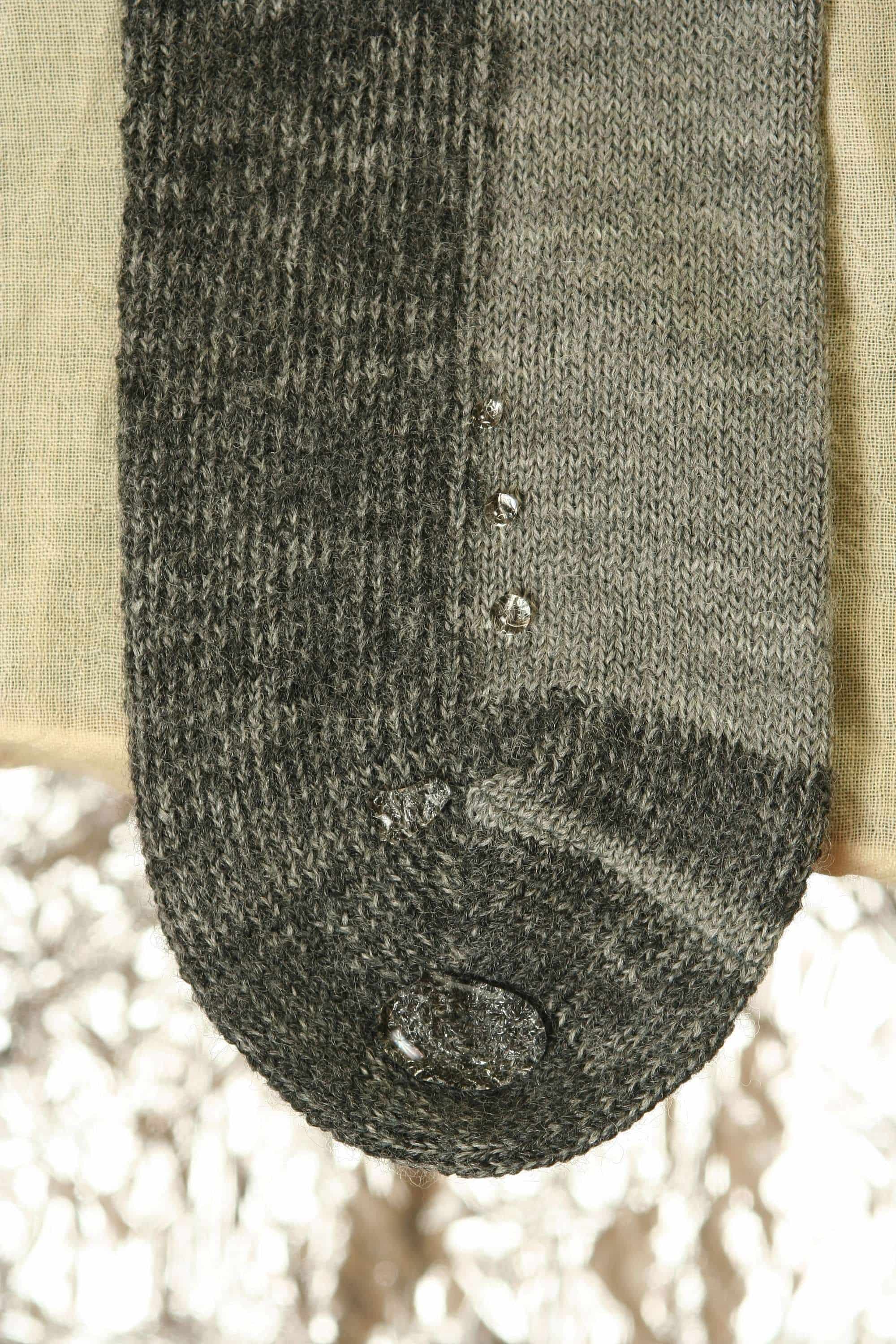 Nahaufnahme von abperlenden Wassertropfen auf grauer Trekking-Socke aus bio Wolle (kbT) und bio Baumwolle (kbA)