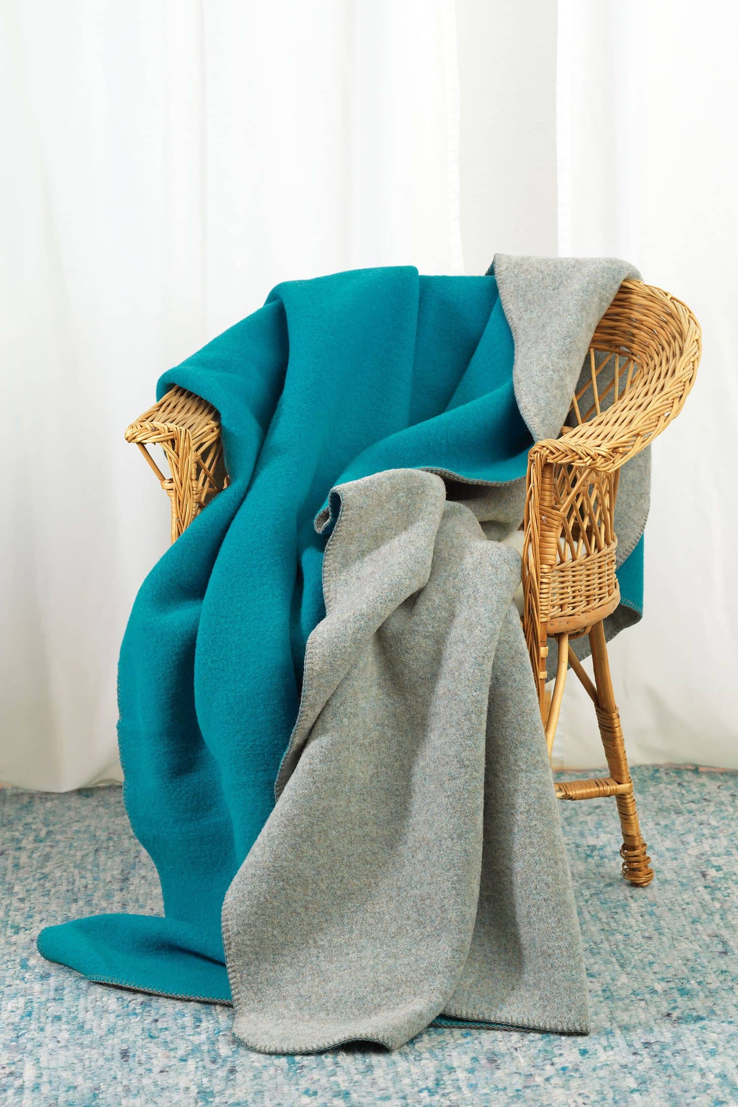Finkhof-Wolldecke Doubleface türkis/grau 150 x 200 cm türkis/graue Finkhof Doubleface Wolldecke aus bio Wolle (kbT) vom Merinolandschaf über Korbstuhl gelegt