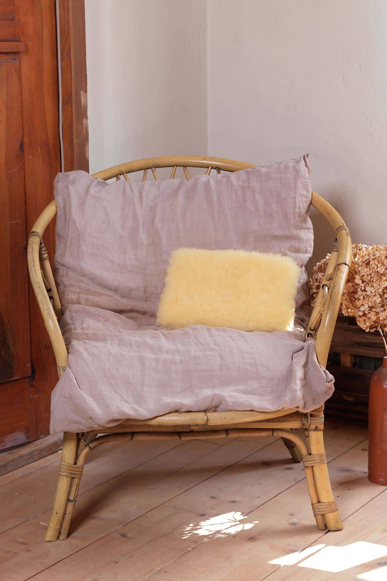 Kuschelkissen aus relugan gegerbtem Finkhof Fell liegt auf einem Korbstuhl